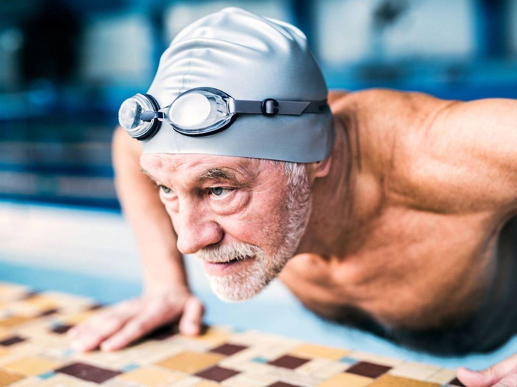 Prostatakrebsvorsorge: Älterer Mann mit Badekappe liegt auf dem Bauch am Schwimmbeckenrand.