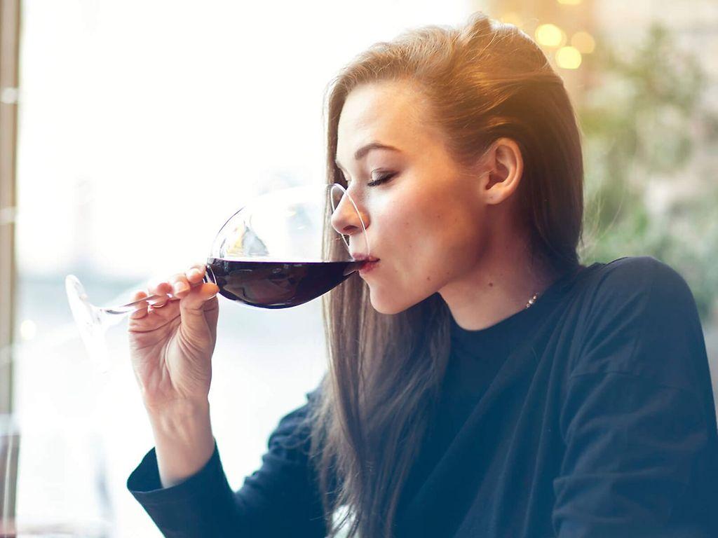 So wirkt Alkohol im Körper: Frau sitzt allein am Tisch und genießt ein Glas Rotwein