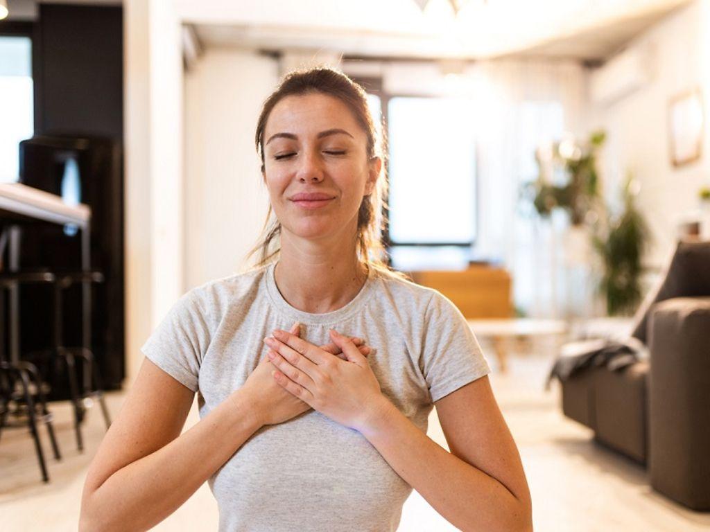 Autogenes Training: Frau mit geschlossenen Augen atmet tief ein und hat ihre Hände auf der Brust.