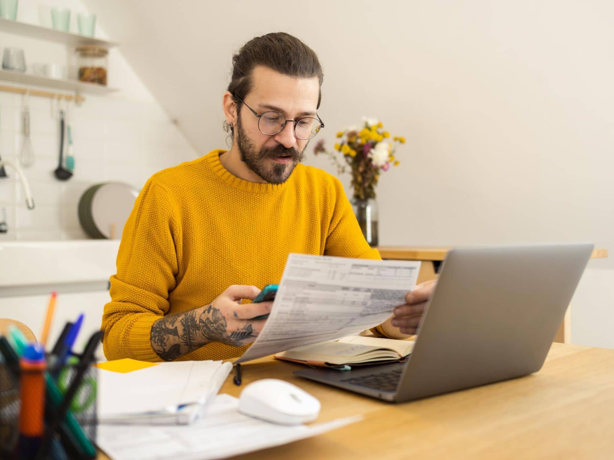 Widersprüche: Ein Mann sitzt in seiner Küche vor einem Notebook und hält ein Anschreiben in der Hand.