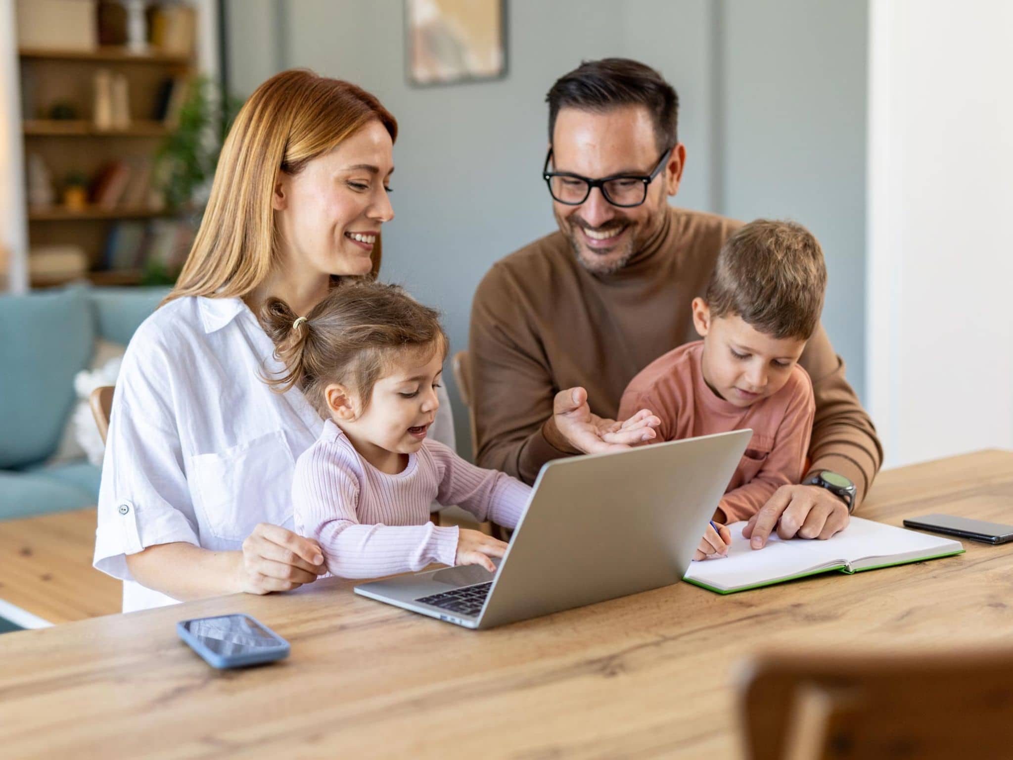 Bonusprogramm: Junge Familie mit zwei Kindern sitzt zuhause gemeinsam vor einem Notebook.