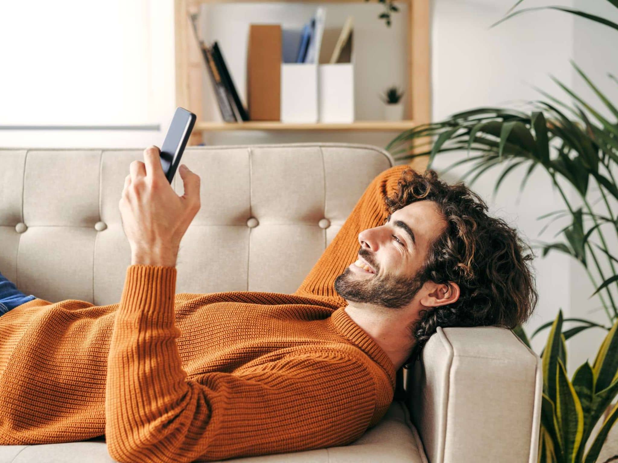 Digitale Angebote: Junger Mann liegt auf dem Sofa und schaut auf sein Handy.