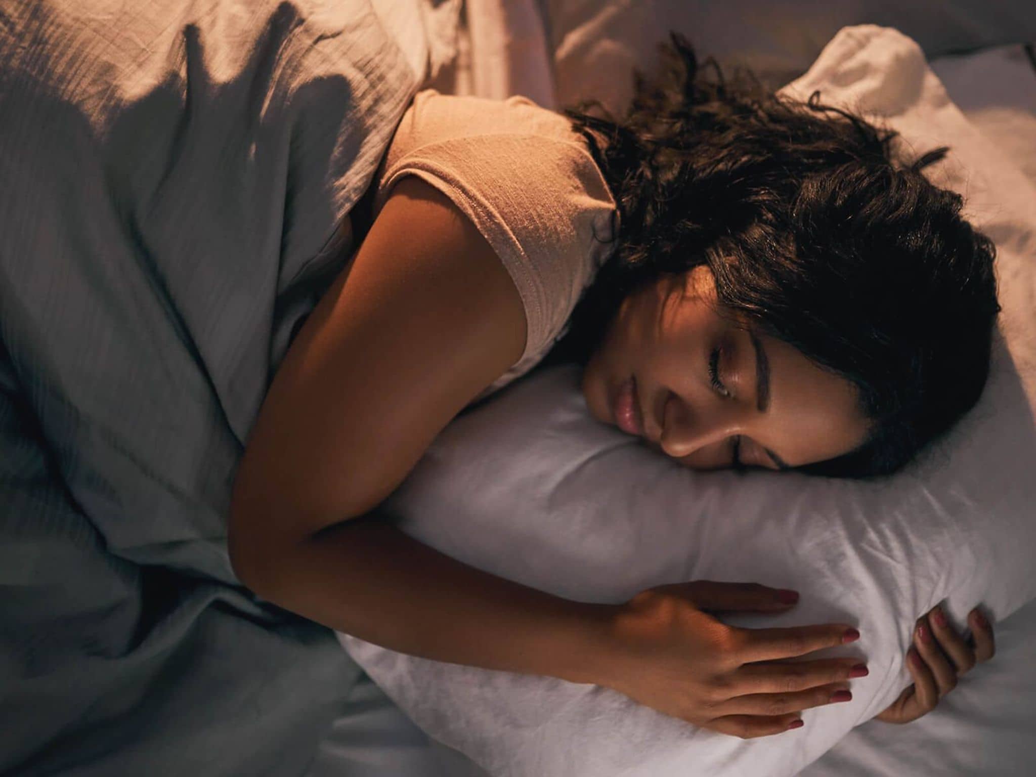 Schlafphasen: Junge Frau, die im Bett schläft und ihr Kissen umarmt