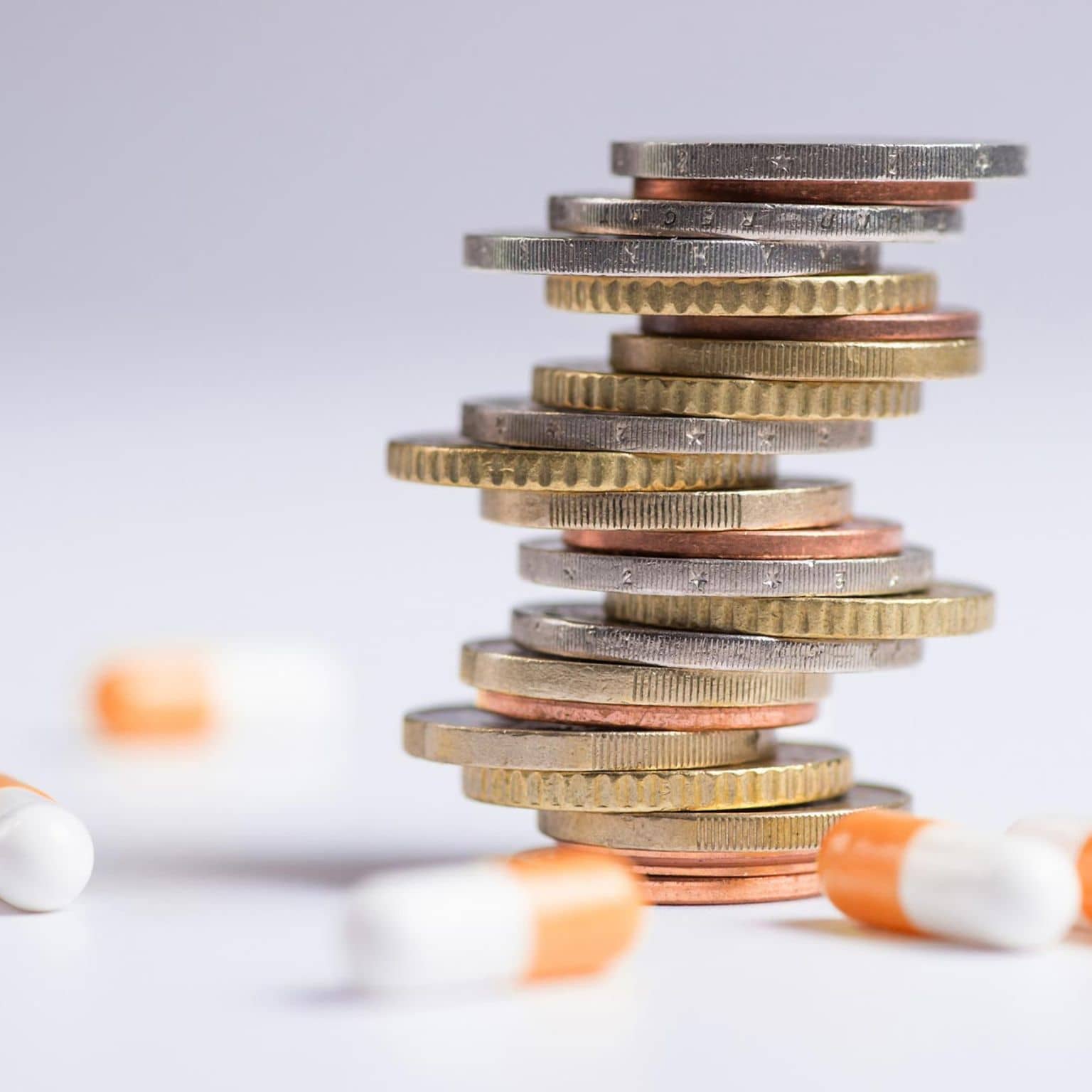 AMNOG-Report 2025: Mehrere Tabletten liegen verstreut um einen Stapel Münzen herum.