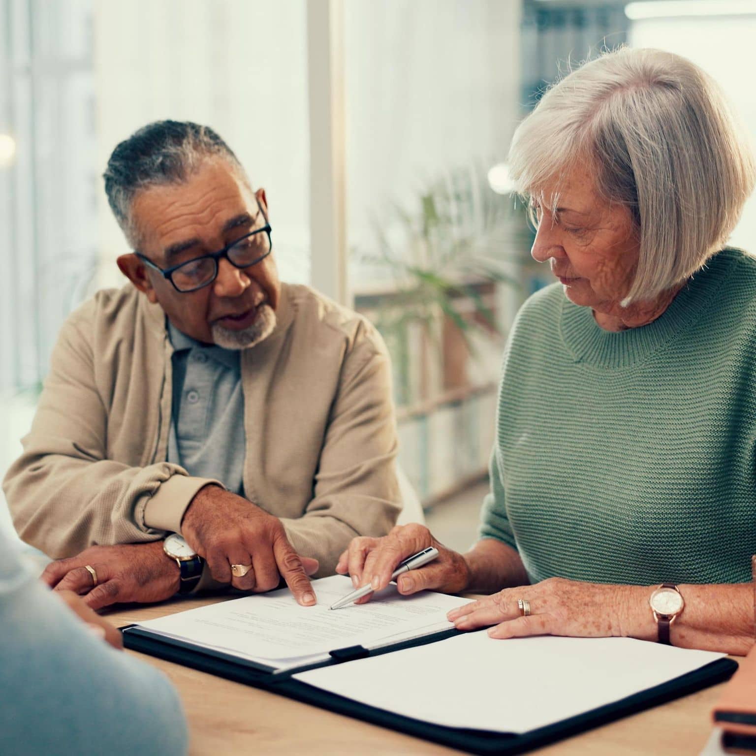 DAK-Pflegereport 2025: Älterer Mann schaut zusammen mit älterer Frau und einem Pflegenden Unterlagen an einem Schreibtisch an.