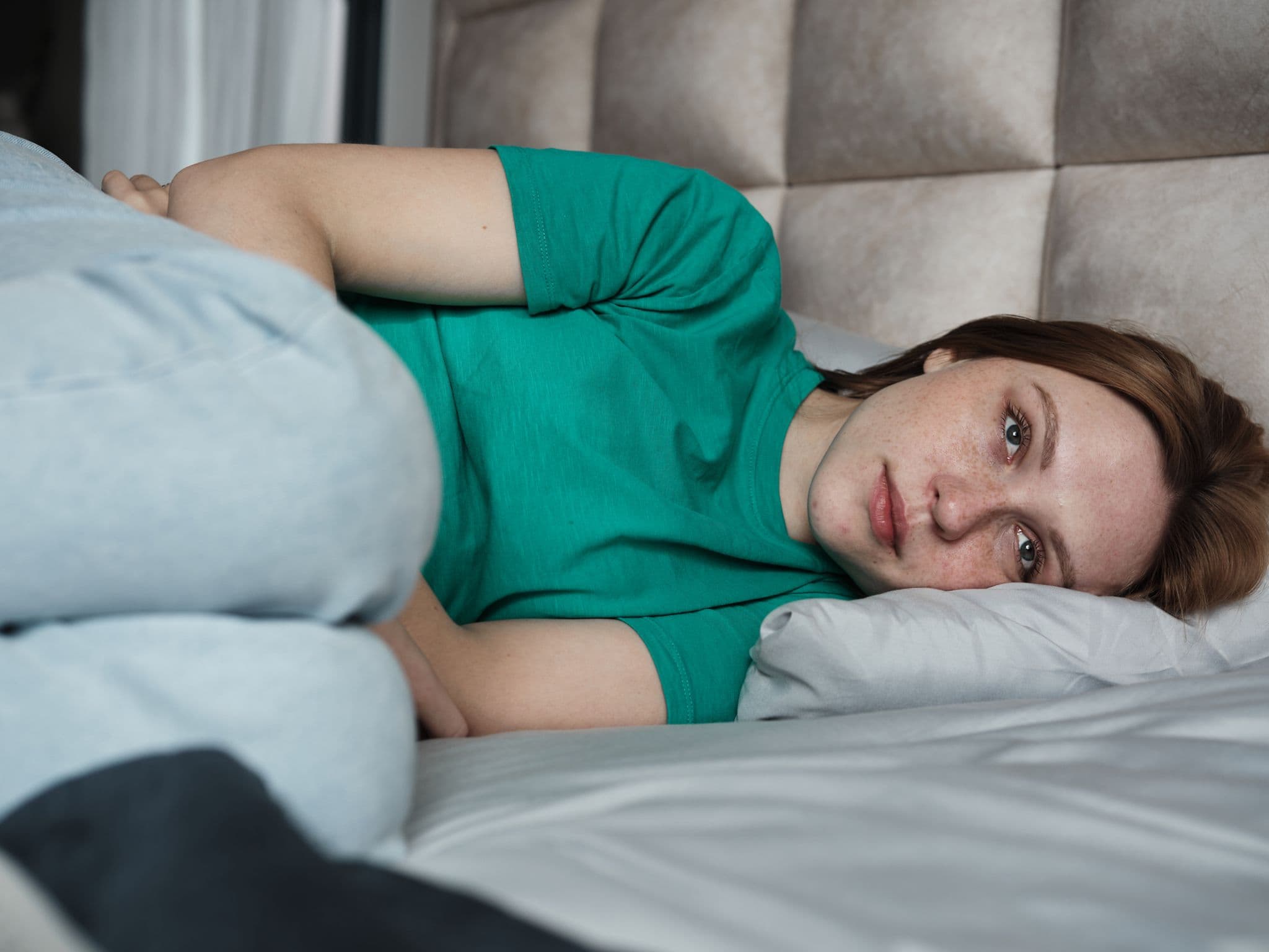 Eine Frau liegt starr im Bett und guckt traurig.