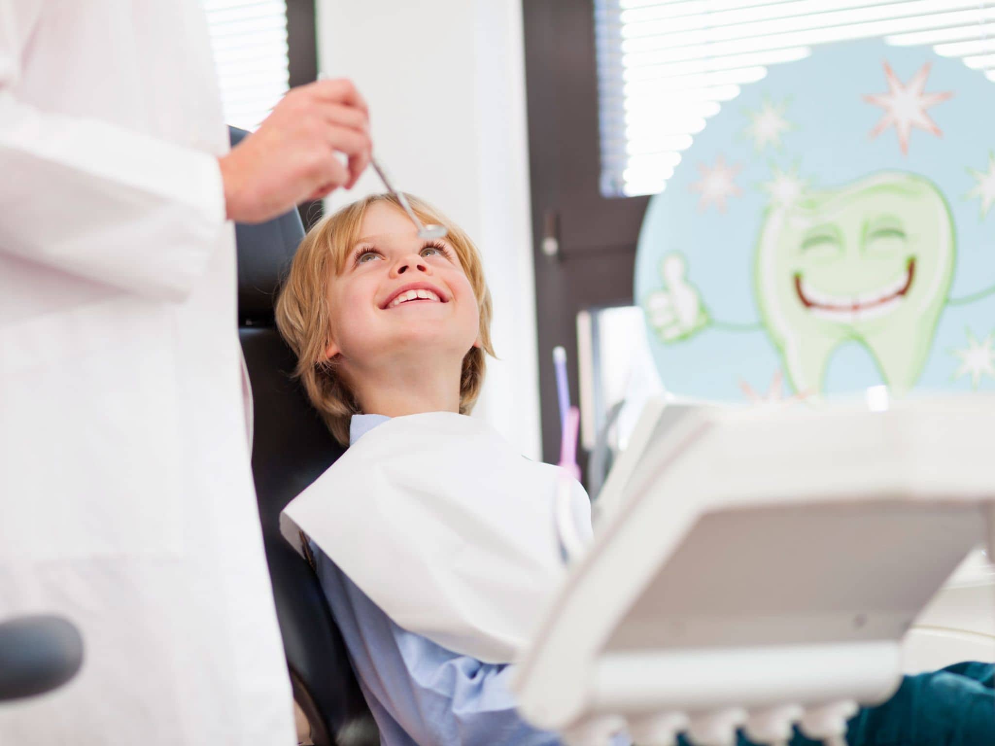Vollnarkose beim Kinderzahnarzt: Fröhlicher Junge sitzt auf dem Behandlungsstuhl beim Zahnarzt.