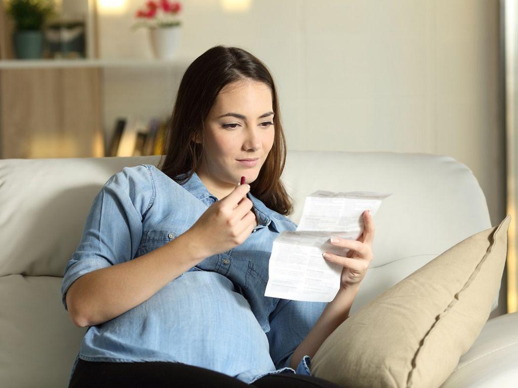 Eisen, Jod und Folsäure: Schwangere hält in der einen Hand Tablette vor dem Mund, in der anderen den Beipackzettel.