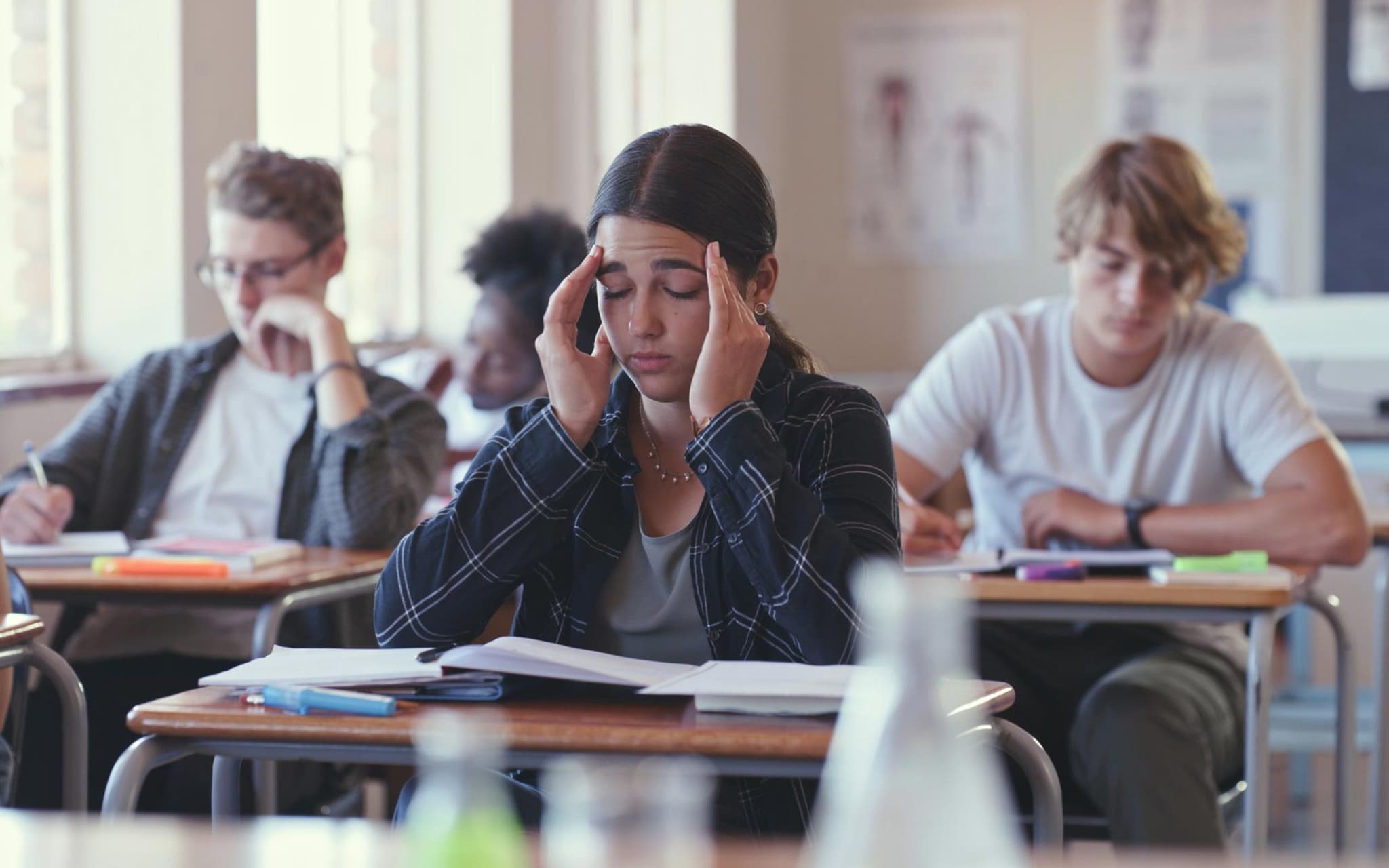 Präventionsradar 2025: Teenagerin sitzt mit geschlossenen Augen in der Schulklasse und hält sich die Hände an die Schläfen.