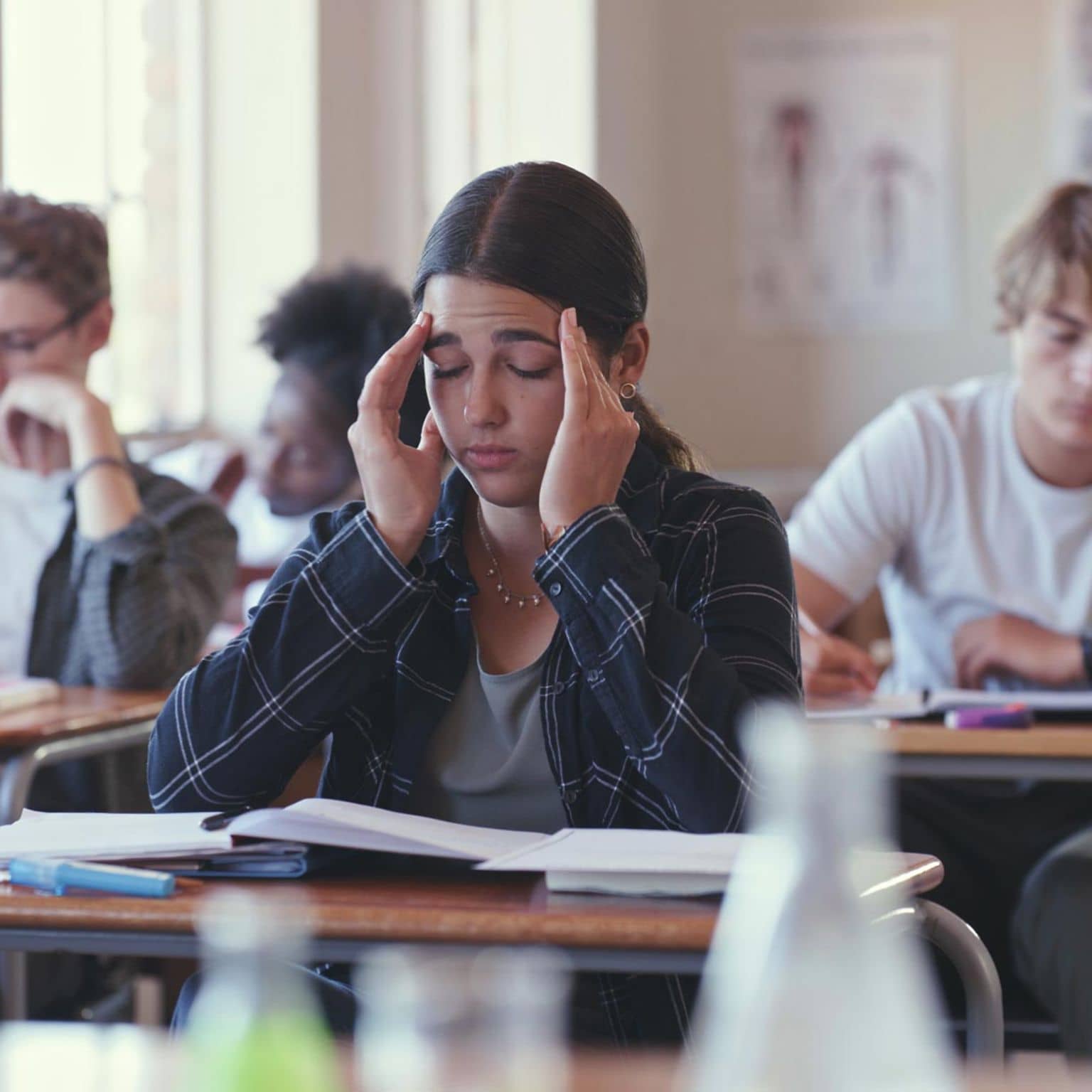 Präventionsradar 2025: Teenagerin sitzt mit geschlossenen Augen in der Schulklasse und hält sich die Hände an die Schläfen.