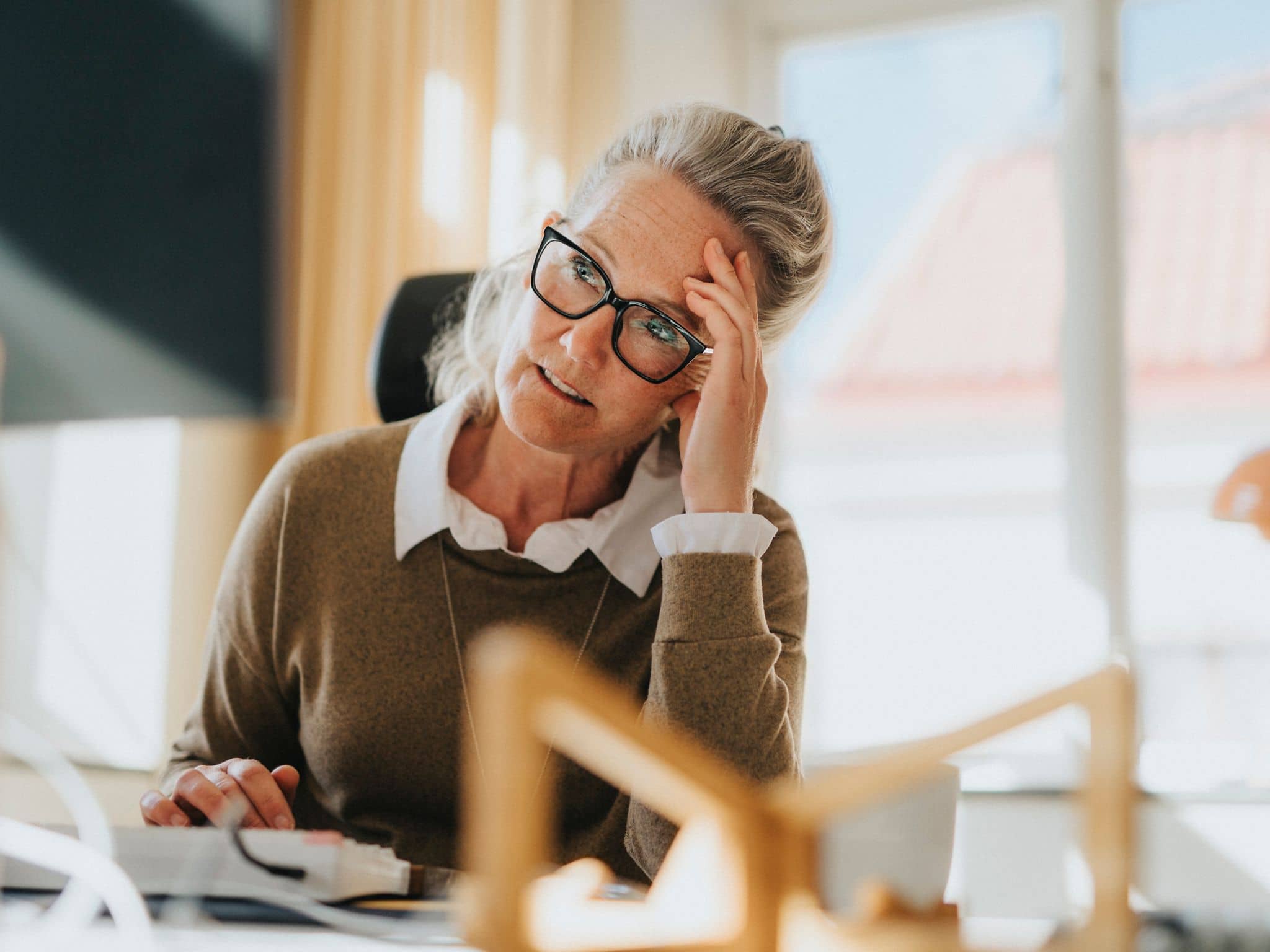 Wechseljahre in Deutschland: Eine ältere Arbeitnehmerin sitzt am Schreibtisch und ist erschöpft