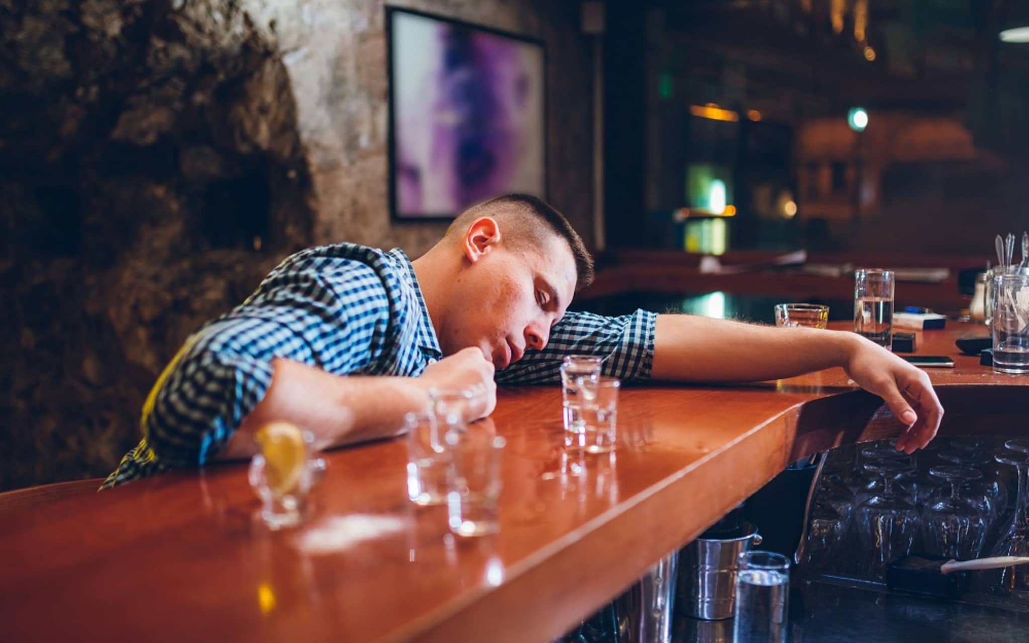Betrunkener Mann liegt mit Kopf auf Bar neben leeren Schnapsgläsern nach starkem Alkoholkonsum.