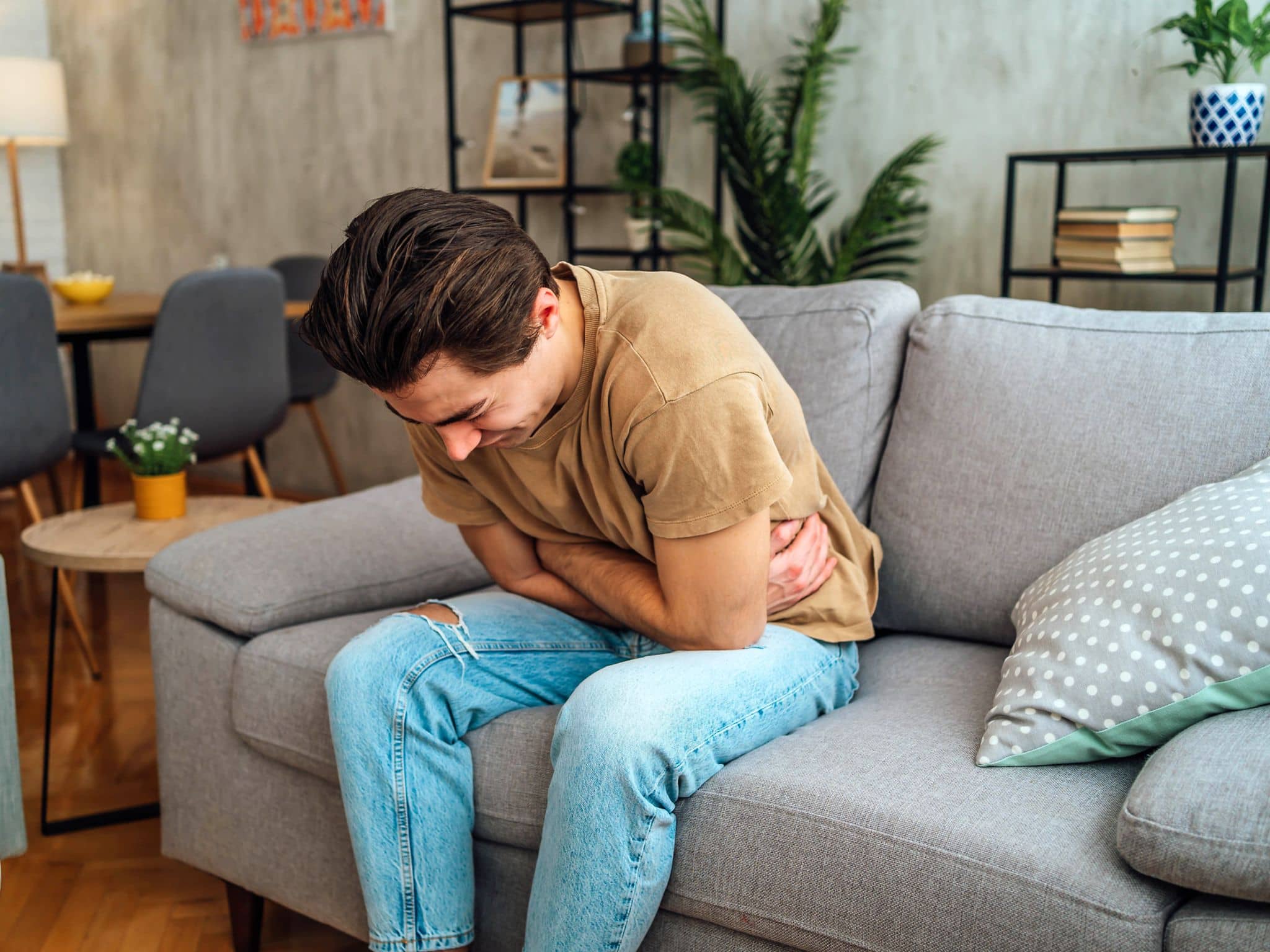 Hodentorsion: Ein Mann sitzt auf einem Sofa und hält sich seinen Bauch vor Schmerzen
