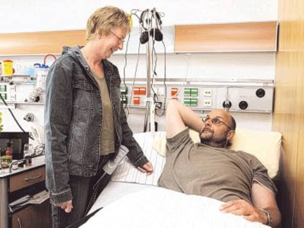 Aufnahme von Patient Hubert Knicker im Krankenbett, seine Frau steht neben ihm.