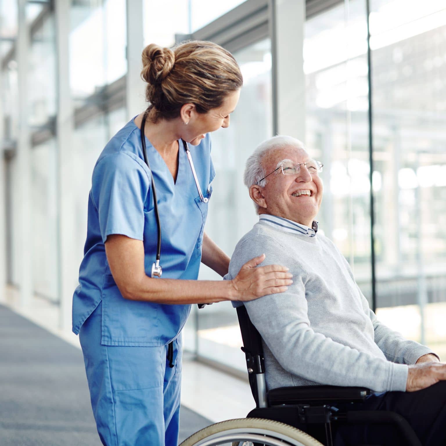 Ein älterer Mann im Rollstuhl wird von einer Pflegerin über einen Flur geschoben