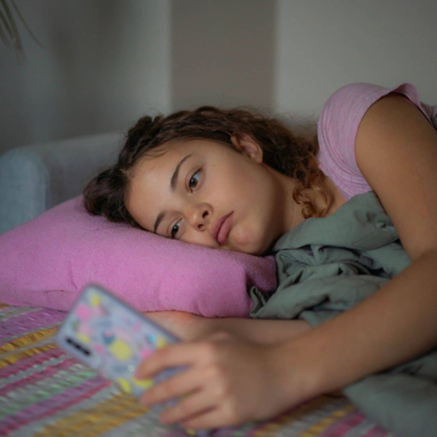 Jugendliche liegt apathisch im Bett und starrt aufs Smartphone.
