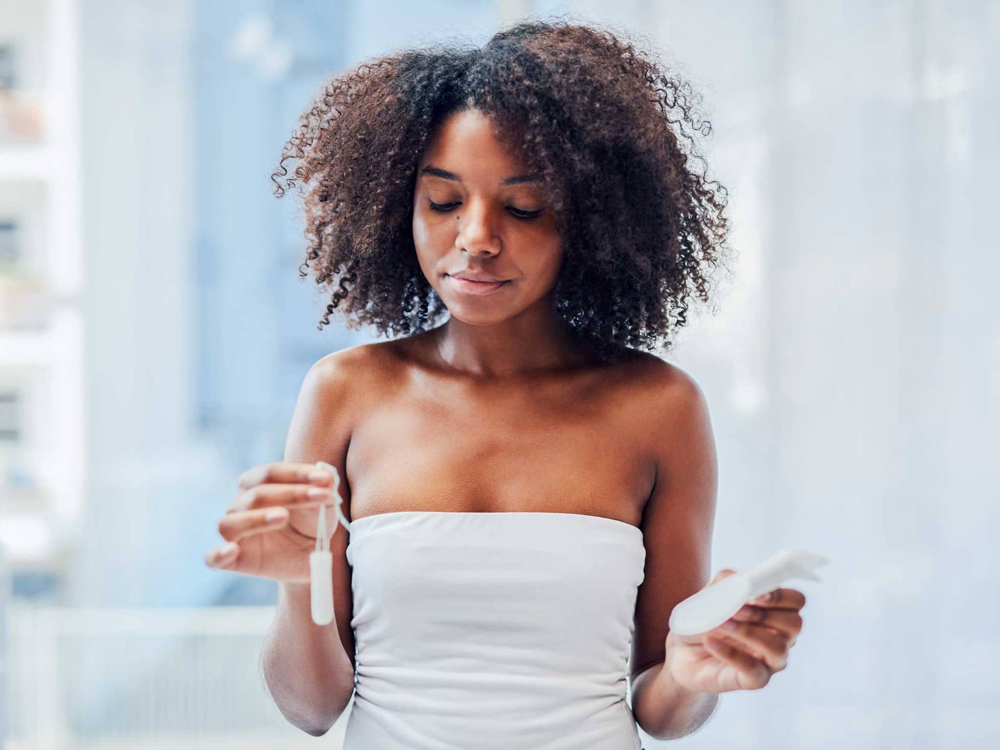 Eine junge Frau hält in der einen Hand ein Tampon hoch, in der anderen eine Binde