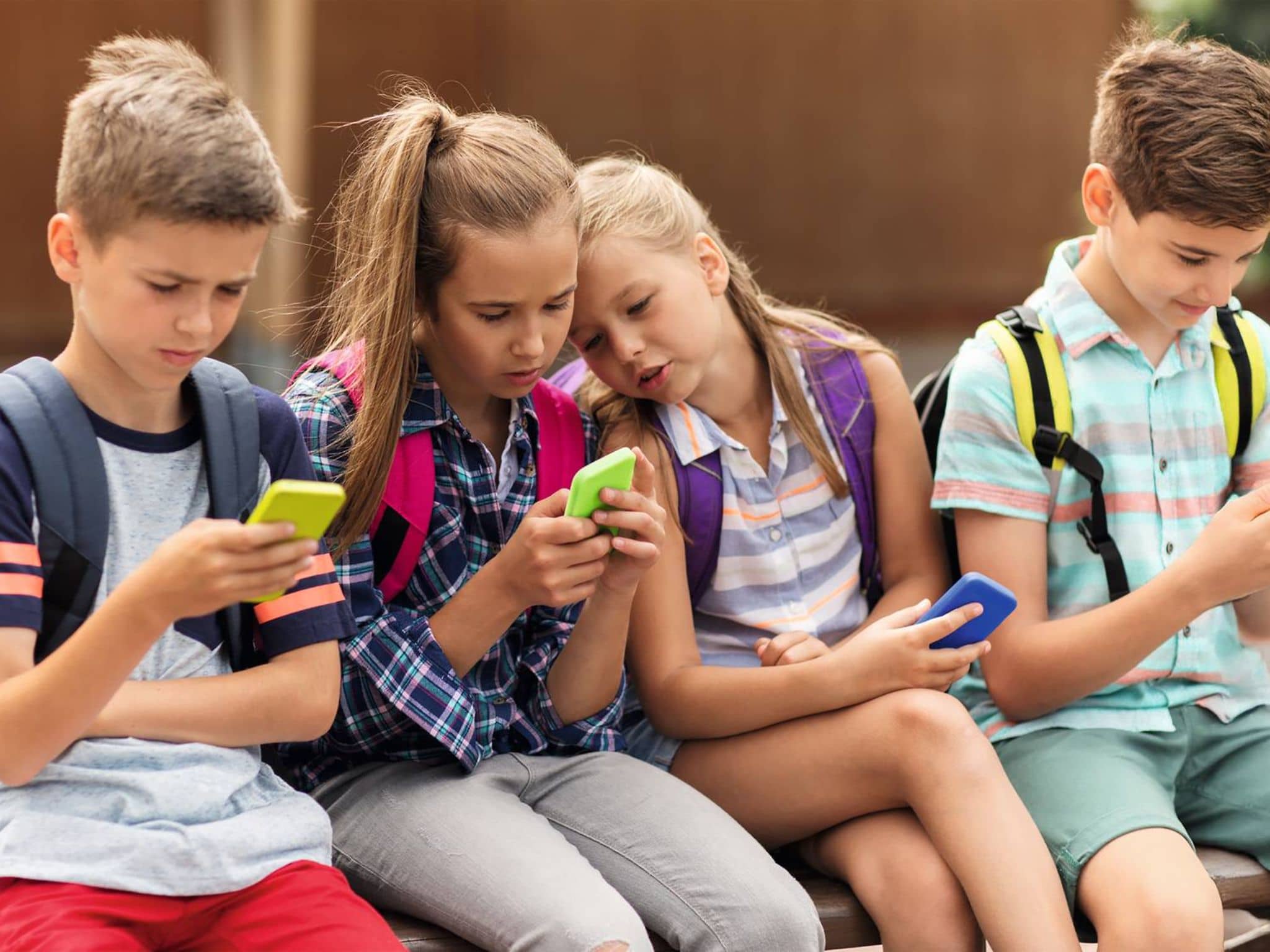 Schulkinder schauen auf ihre Handys.