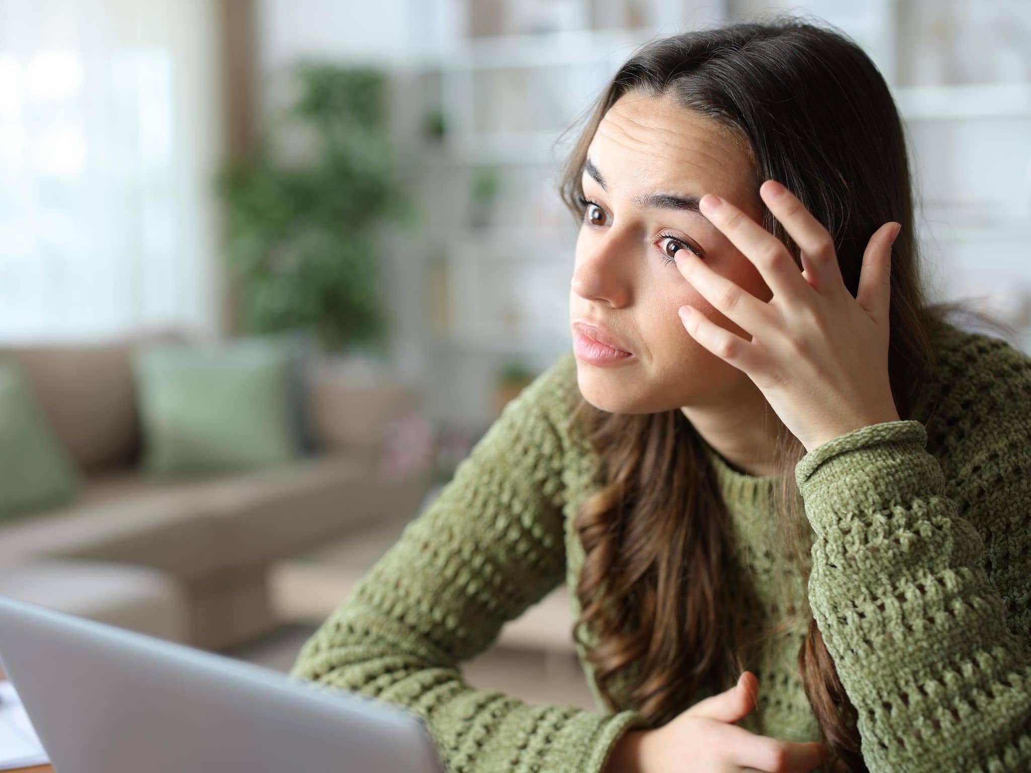 Frau fasst sich ins Auge während sie vorm Laptop sitzt.