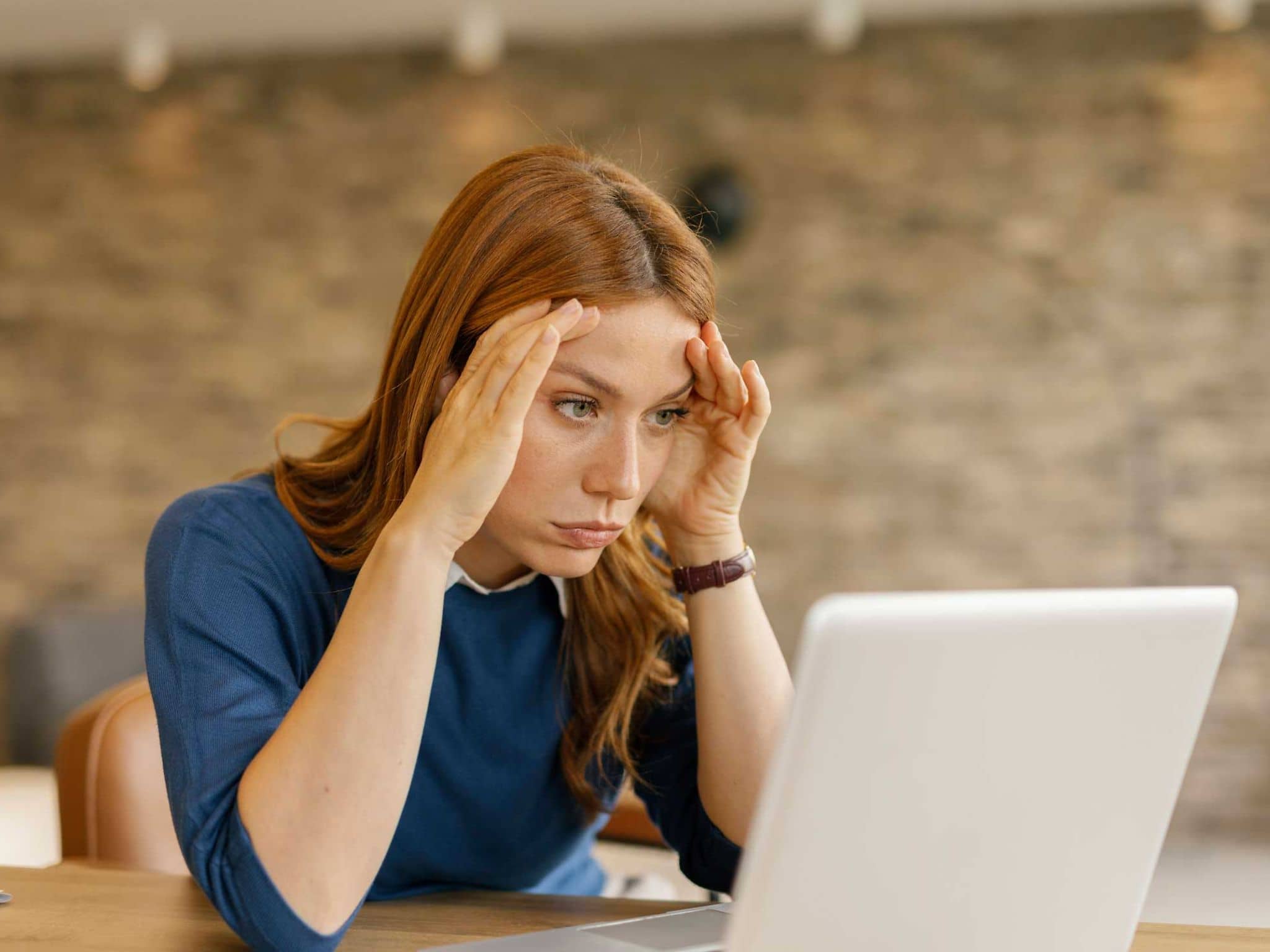 Junge Frau fasst sich erschöpft ins Gesicht und schaut auf einen Laptop