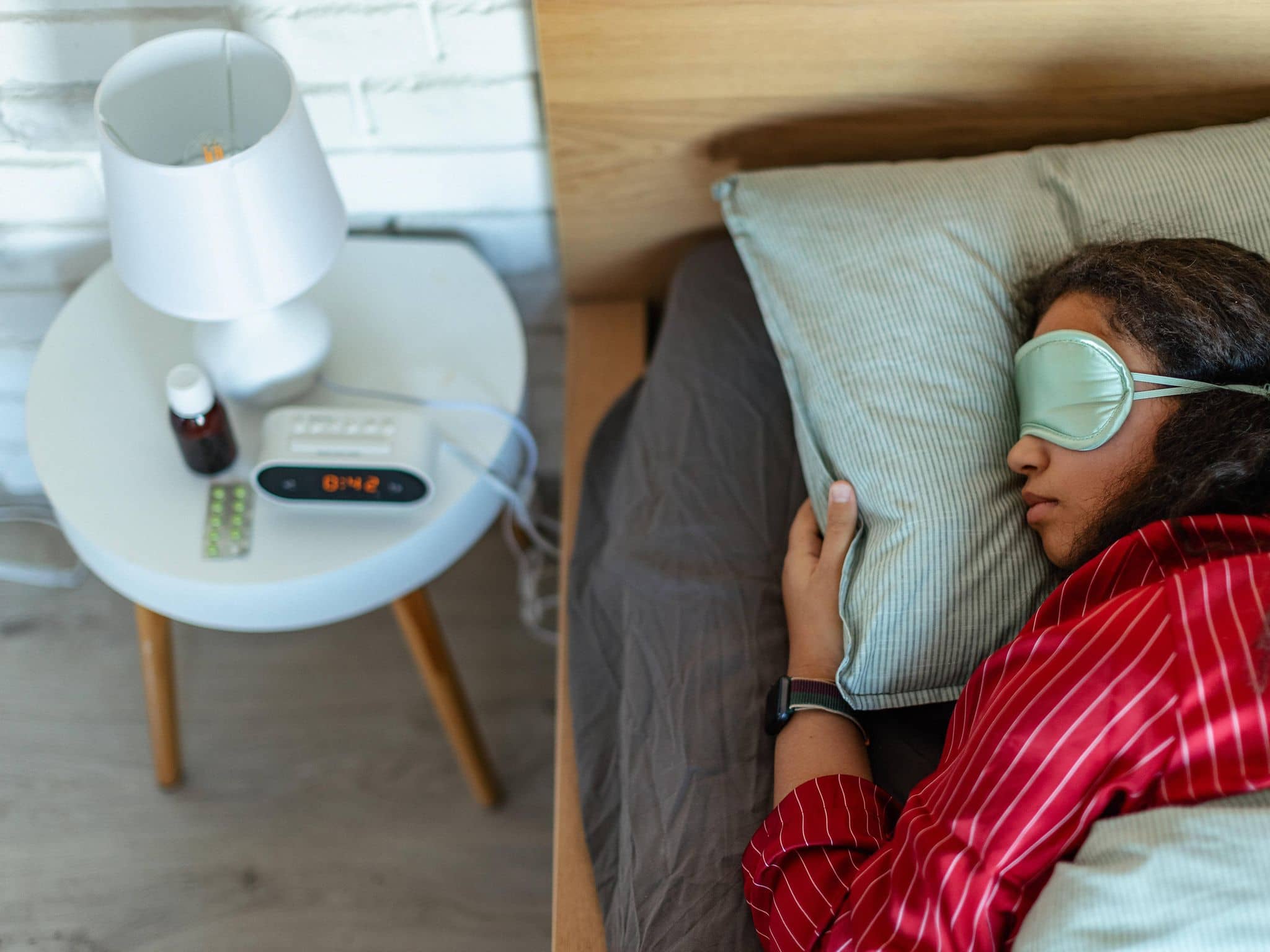 Eine Frau liegt schlafend im Bett, auf dem Nachttisch sieht man Melatonin-Präparate, die beim Einschlafen helfen sollen.
