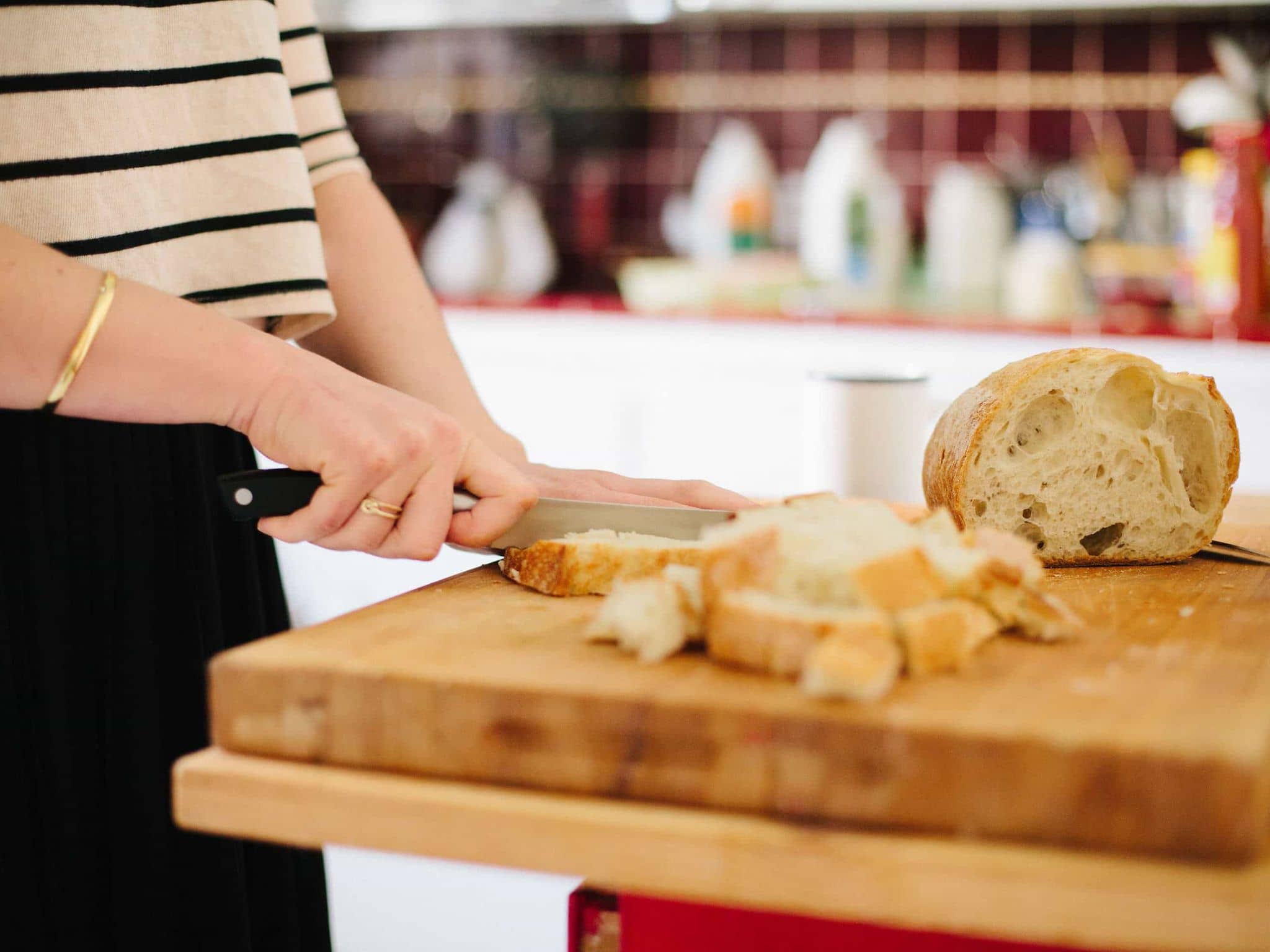 Lebensmittelunverträglichkeiten: Frauenhände schneiden Weizenbrot auf einem Holzbrett.