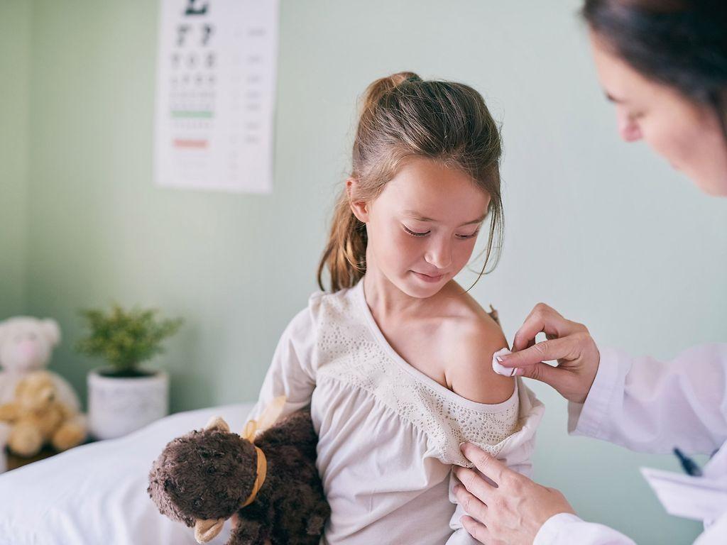 Bild: Impfungen für Kinder: Ärztin tupft Schulter eines Mädchens ab und bereitet sie für Injektion vor.