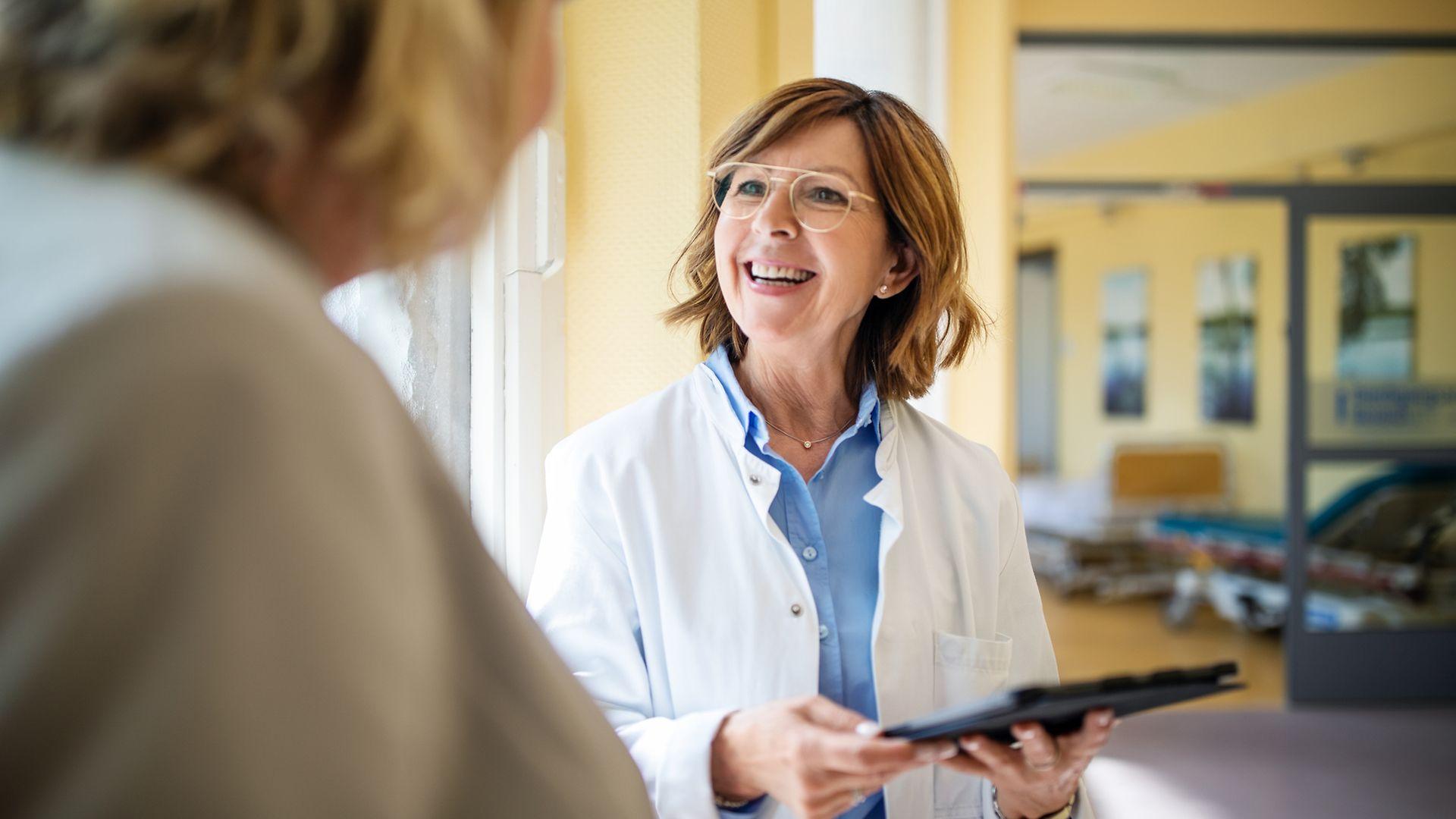 Bild: Ärztin mit Brille und Klemmbrett lächelt ihre Patientin an.