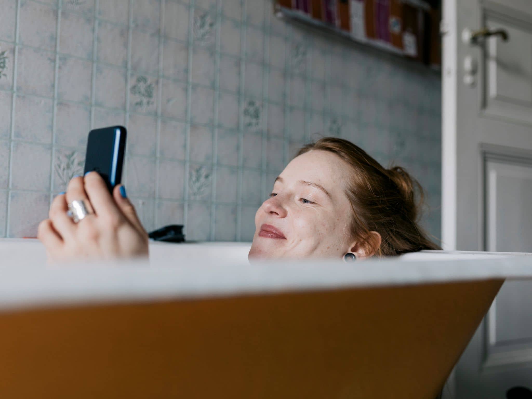 Frau liegt mit Smartphone in der Badewanne