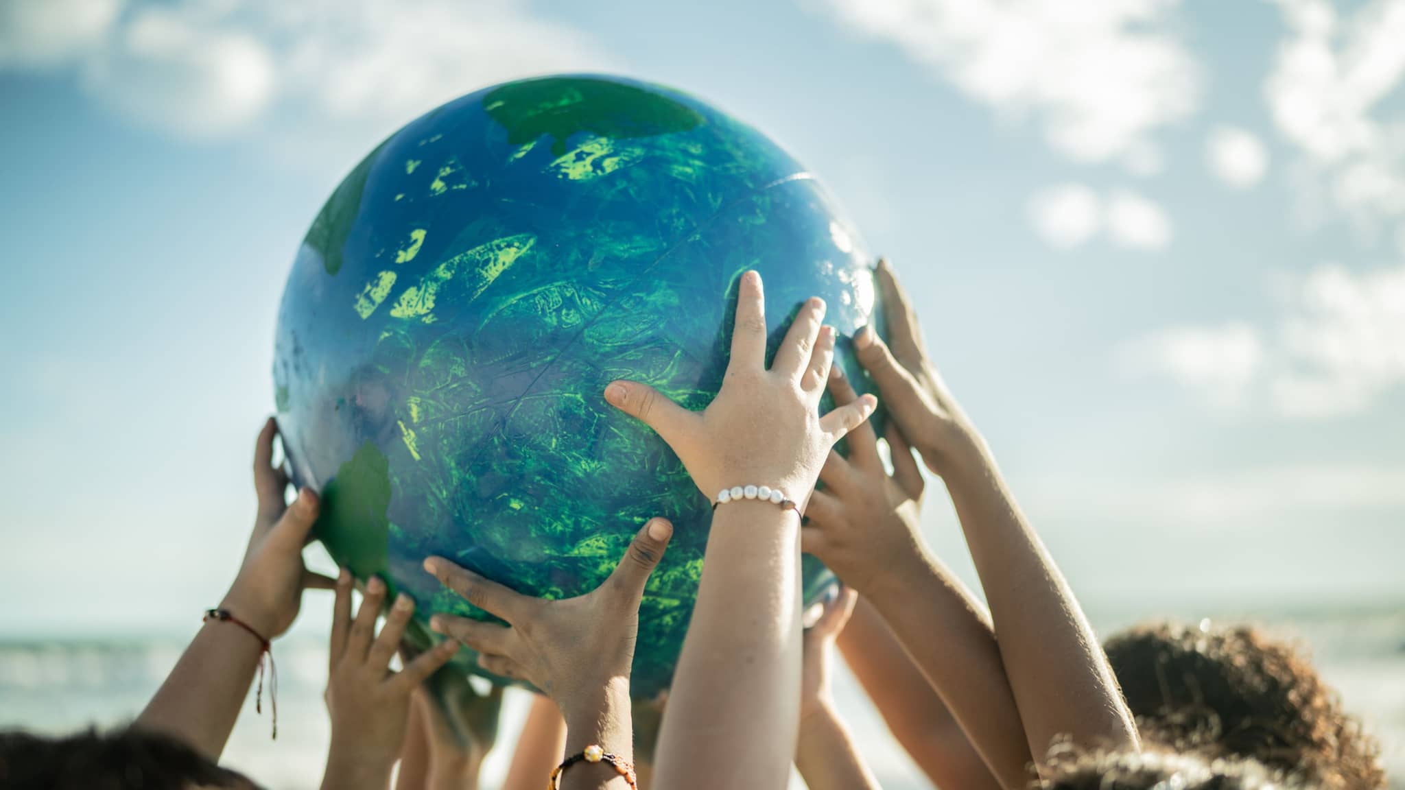 Nachhaltigkeit: Am Strand halten mehrere Kinder einen großen Ball nach oben, der an einen Planeten erinnert.
