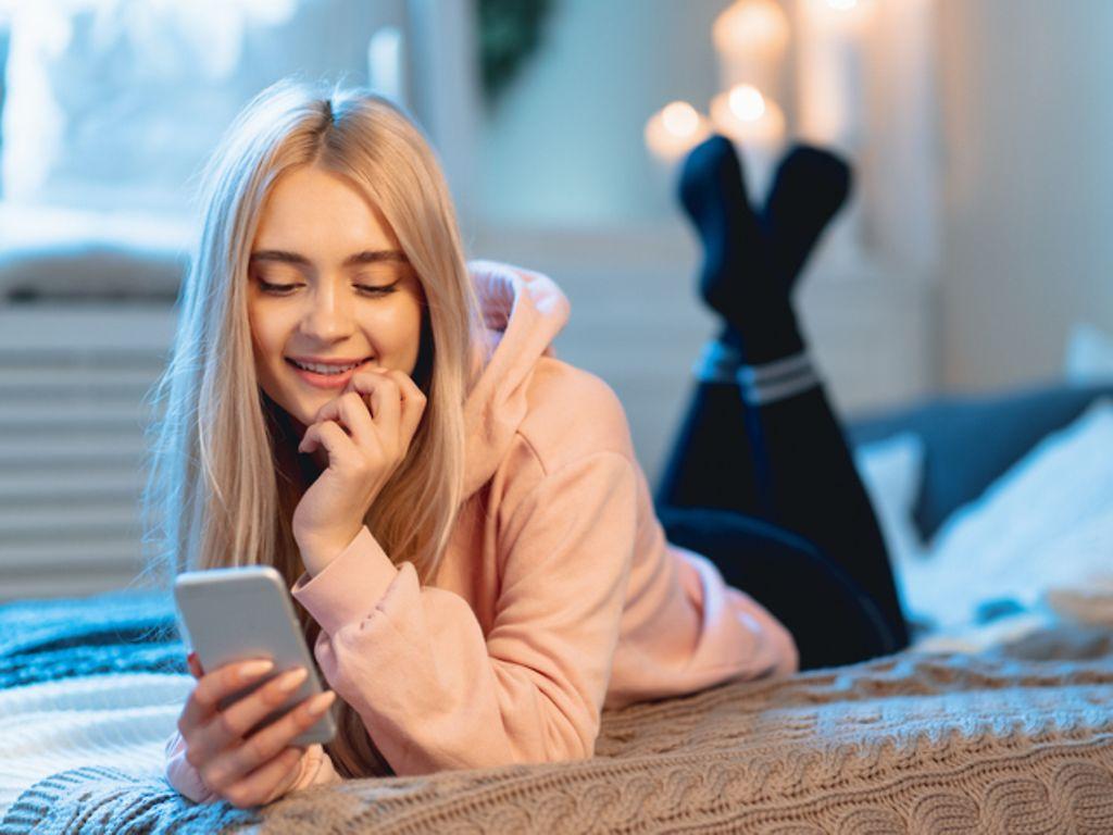 Symbolbild Anatomie der Frau: Ein junges Mädchen liegt auf dem Bett und liest am Smartphone