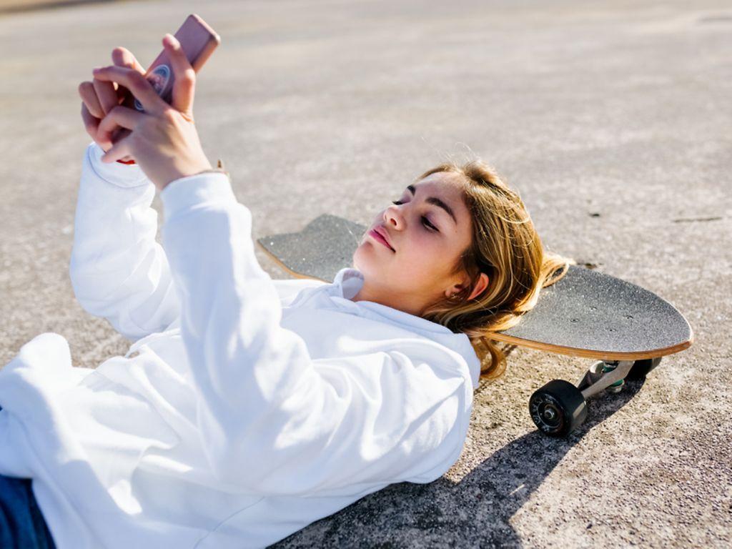 Symbolbild für Schweigepflicht: Ein Teenager-Mädchen macht ein Selfie auf dem Skateboard