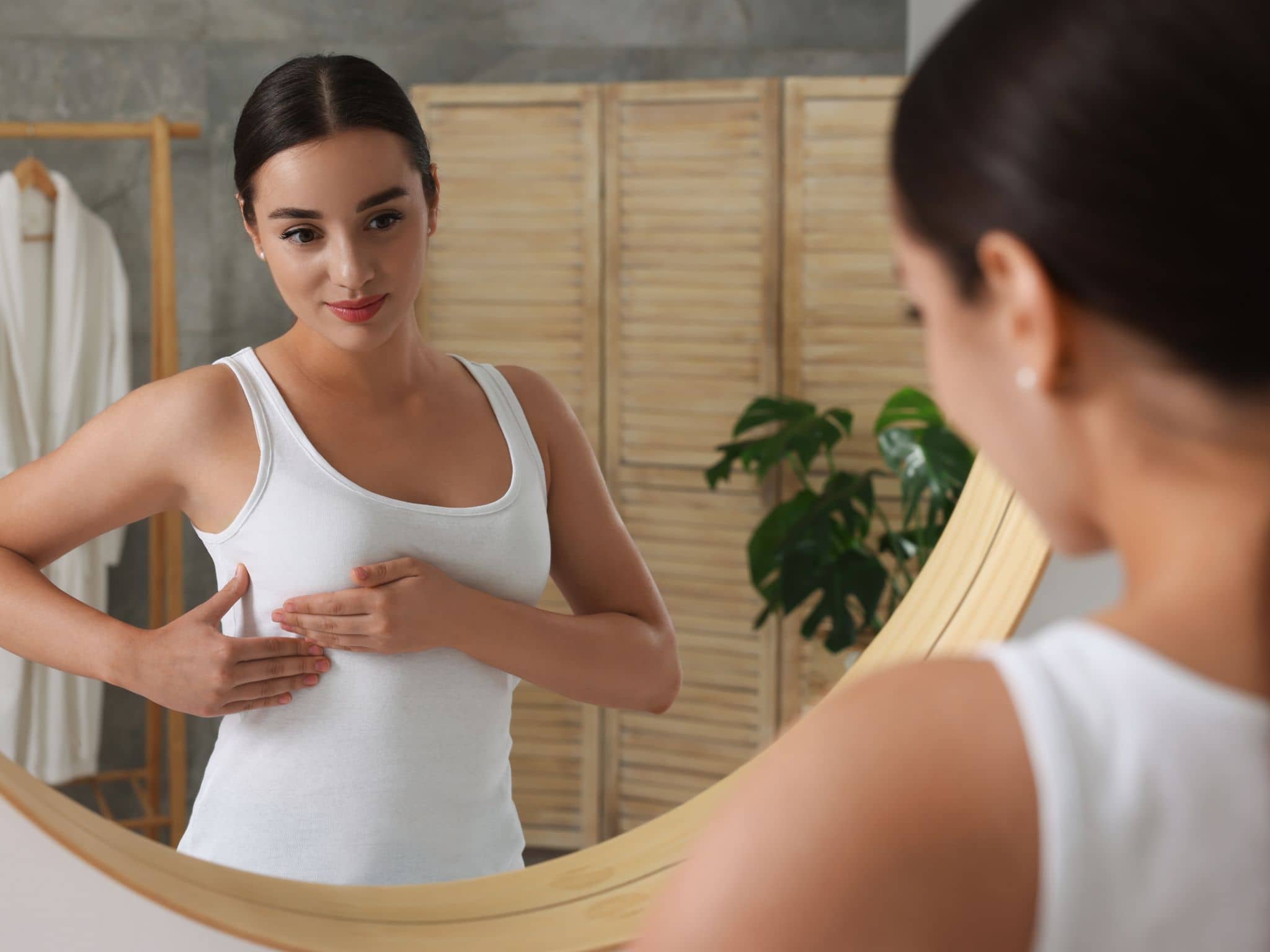 Brust abtasten: Eine Frau steht vor dem Spiegel und tastet ihre Brust ab