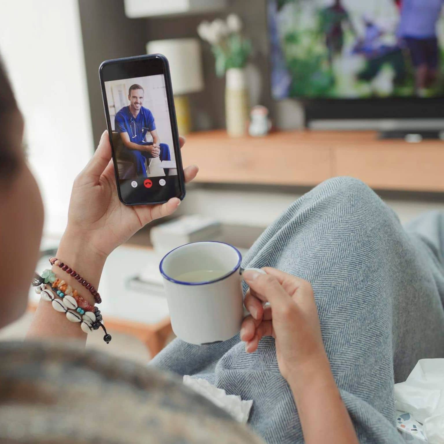 Bild: Frau sitzt auf dem Sofa zuhause und nutzt die Videosprechstunde.
