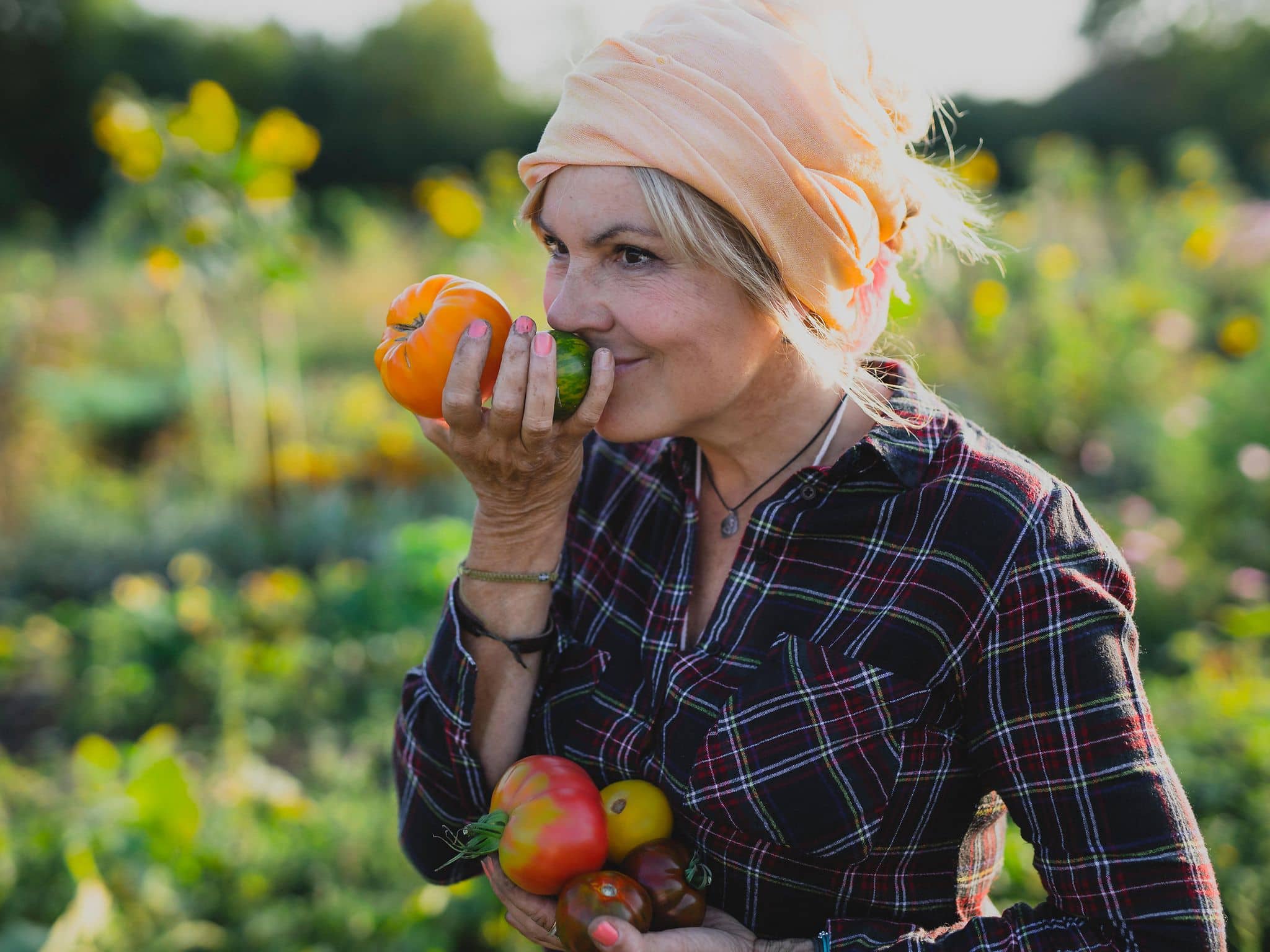 Eine Frau im mittleren Alter steht in einem Gemüsefeld und riecht an Tomaten