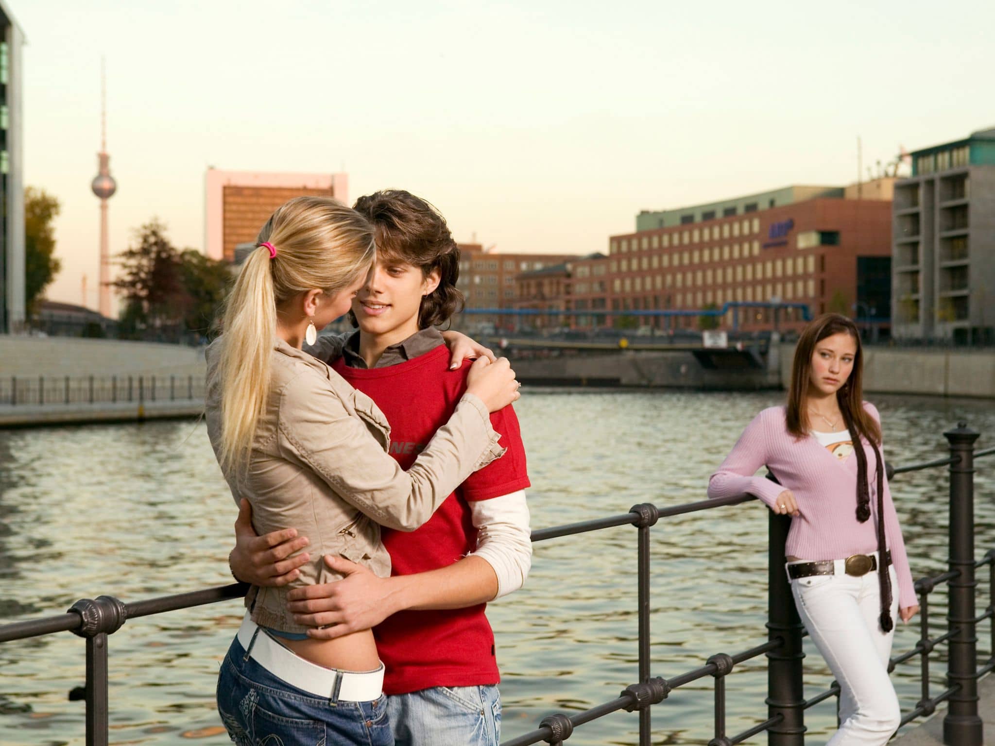 Symbolbild für Eifersucht: Ein junger Mann unterhält sich mit einer jungen Frau und eine andere junge Frau guckt eifersüchtig
