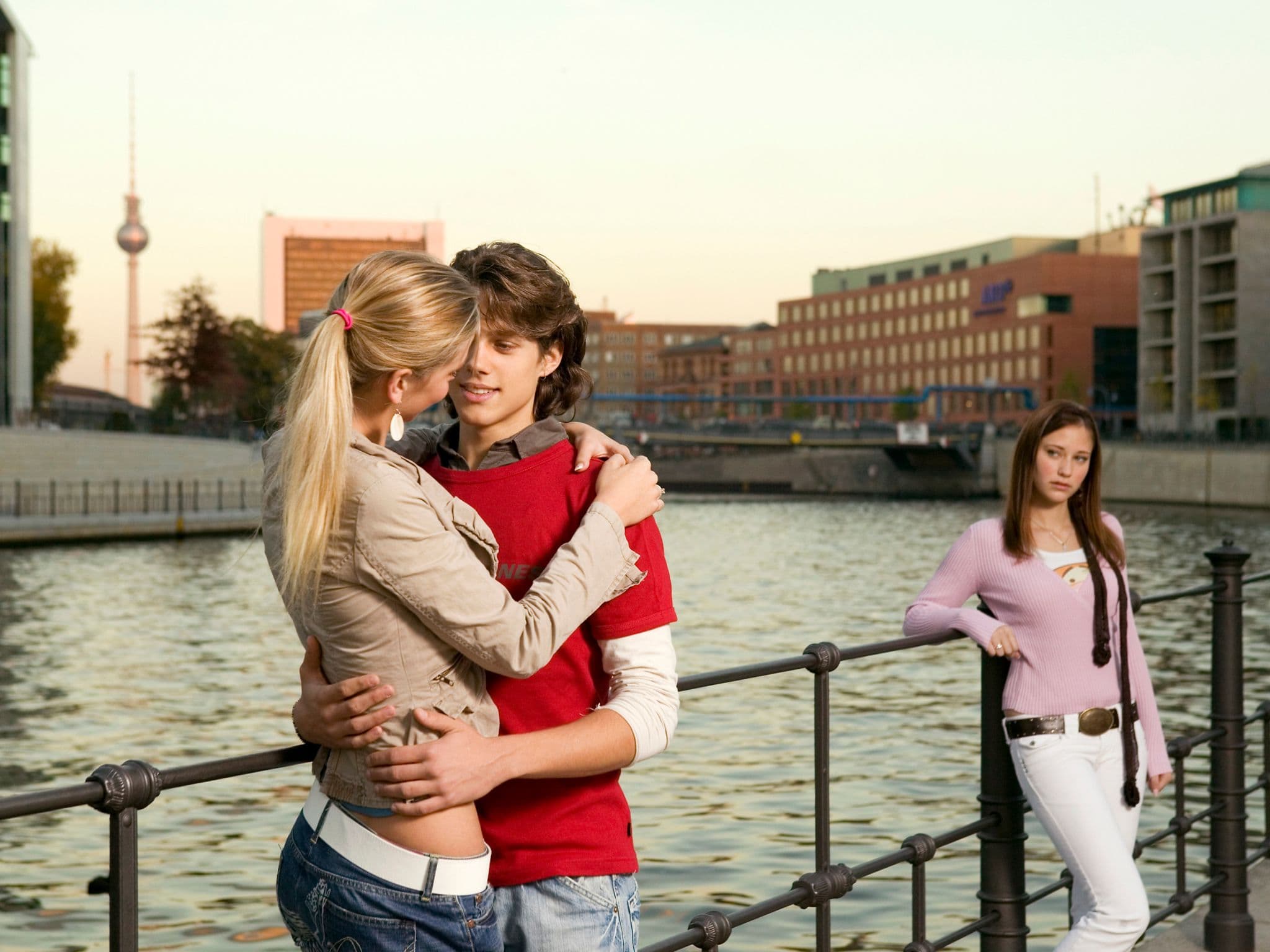 Symbolbild für Eifersucht: Ein junger Mann unterhält sich mit einer jungen Frau und eine andere junge Frau guckt eifersüchtig