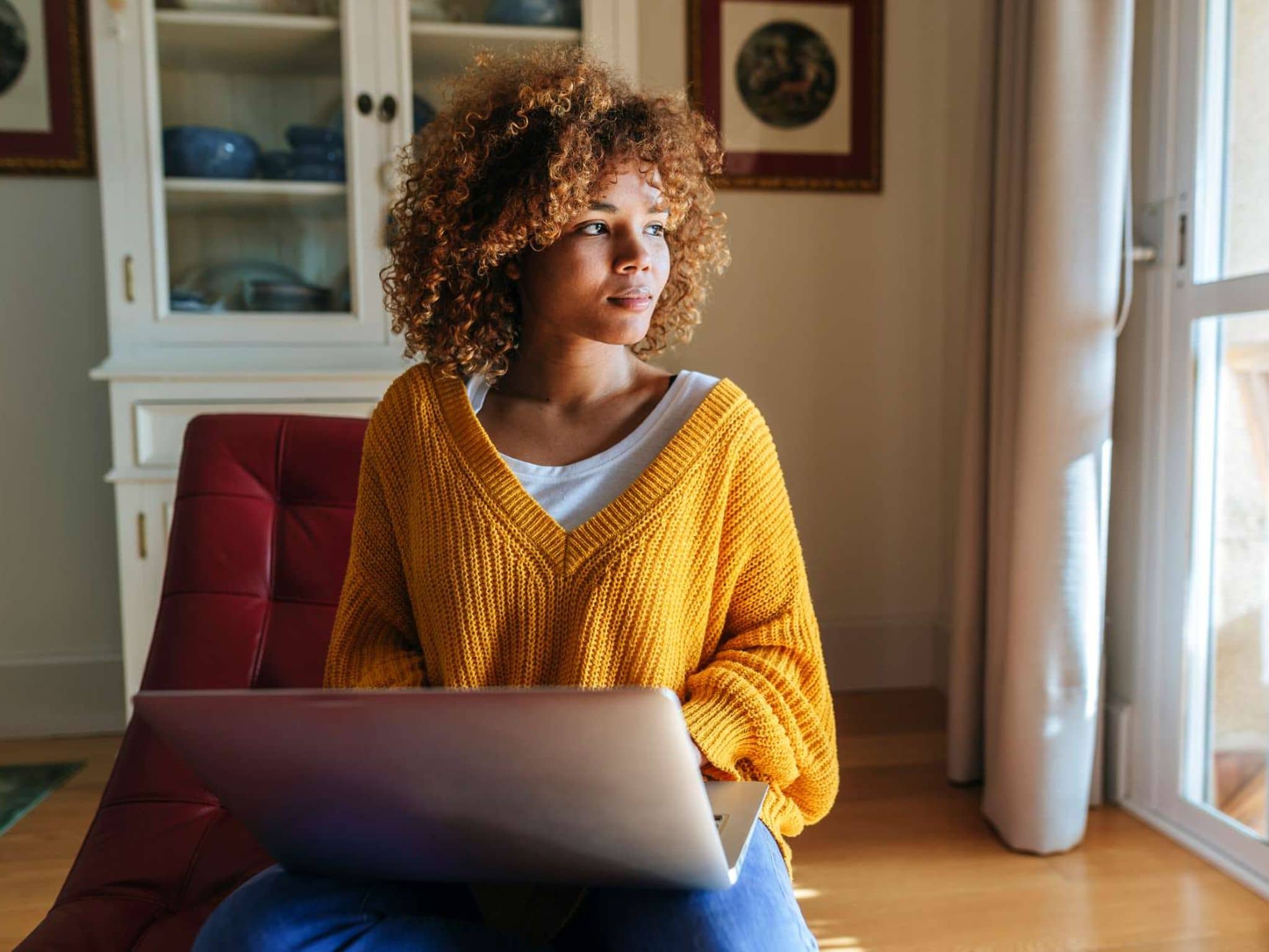 CIRS: Junge Frau sitzt zuhause vor ihrem Notebook und schaut aus dem Fenster.