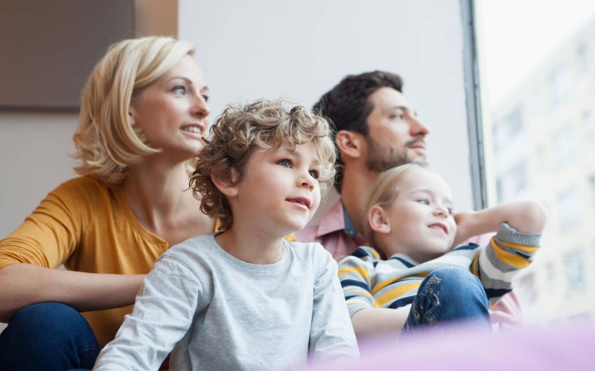 Familie mit zwei kleinen Kindern schaut gemeinsam aus dem Fenster.
