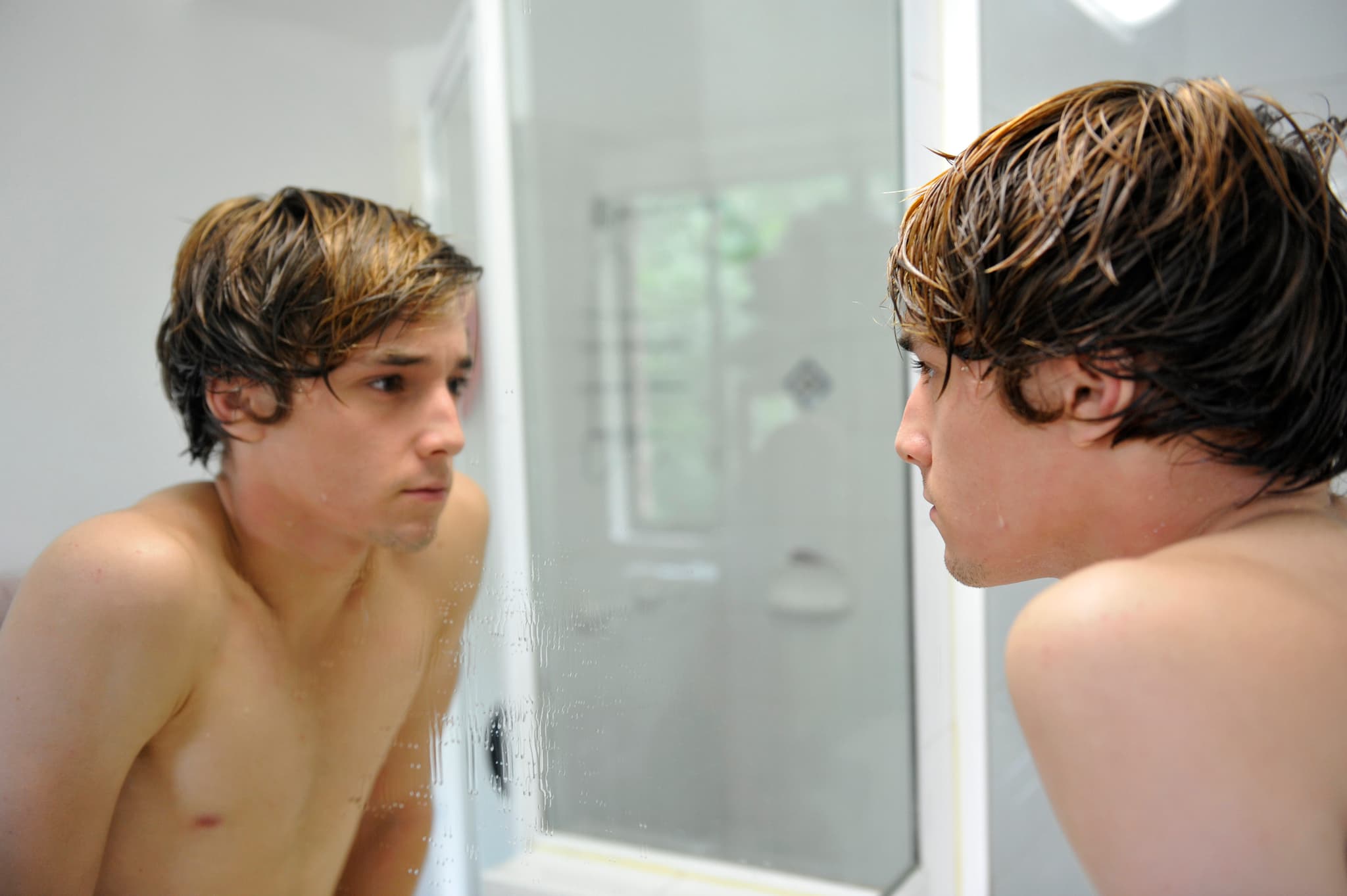 Symbolbild Penisgröße: Teenager betrachtet sich nachdenklich im Spiegel
