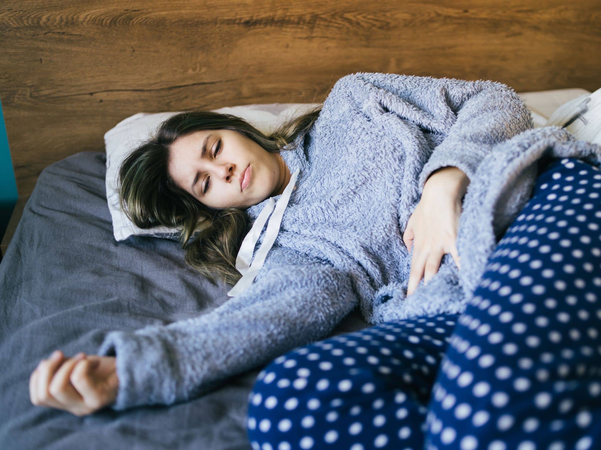 Lichen Sclerosus: Junge Frau liegt betrübt im BEtt und hält ihren Bauch fest.