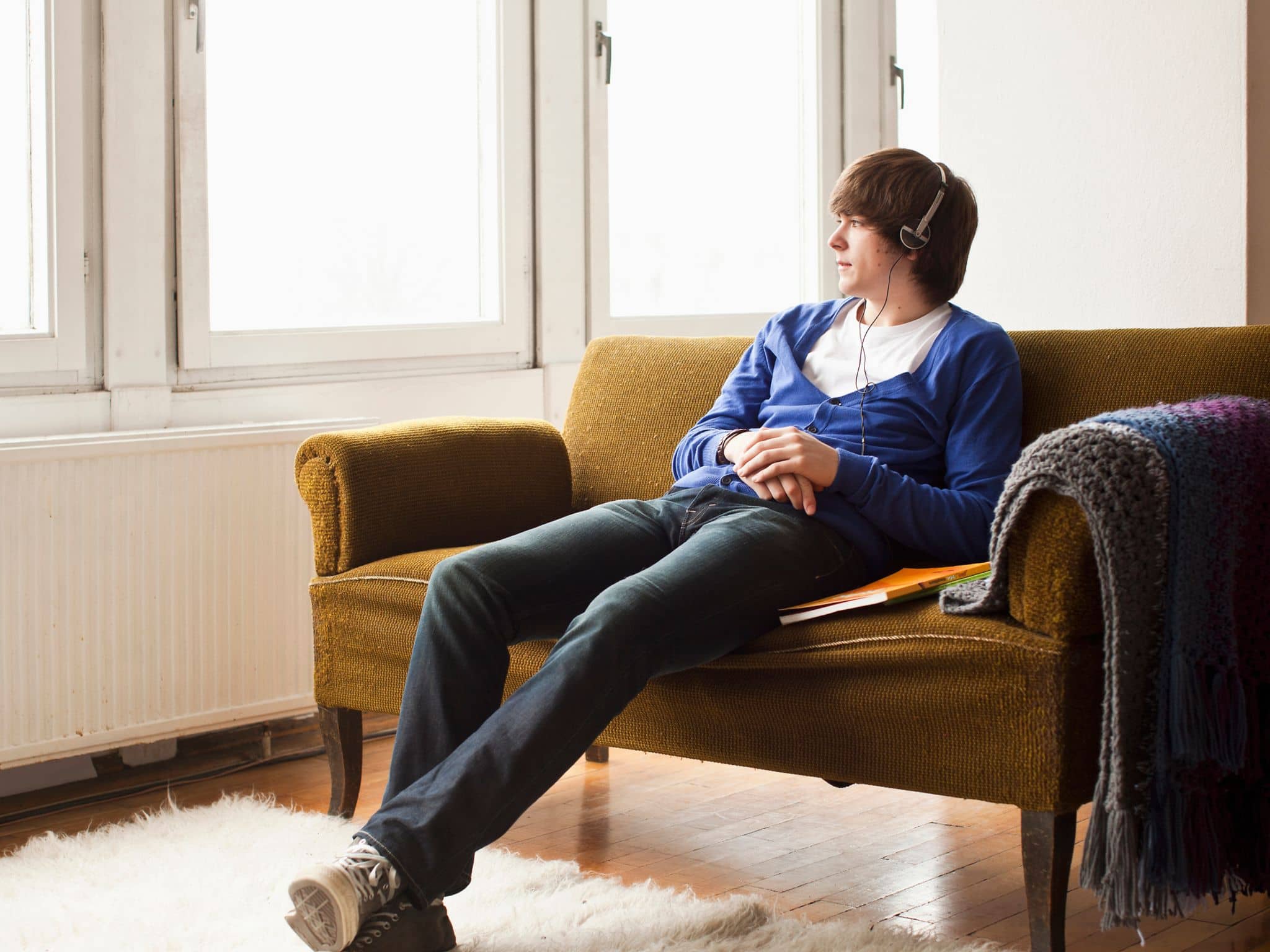 Symbolbild für Schmerzen am Penis: Ein junger Mann sitzt auf dem Sofa hört Musik und chillt