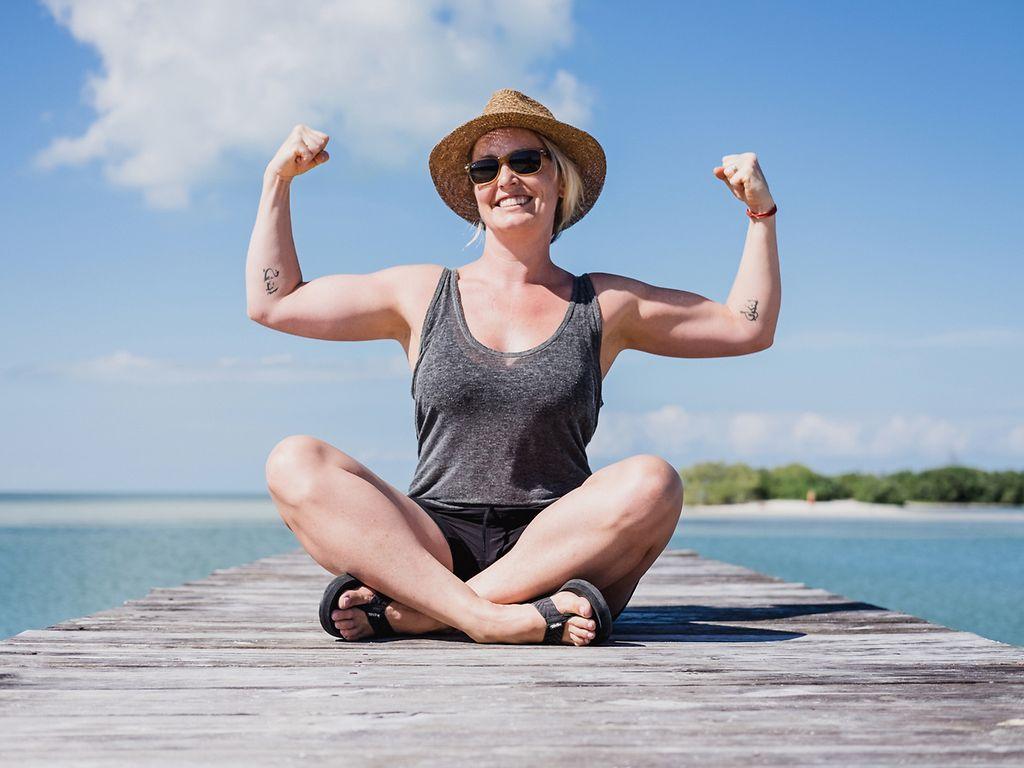 Mind-Muscle-Connection: Glückliche Frau, die ihre Armmuskeln anspannt