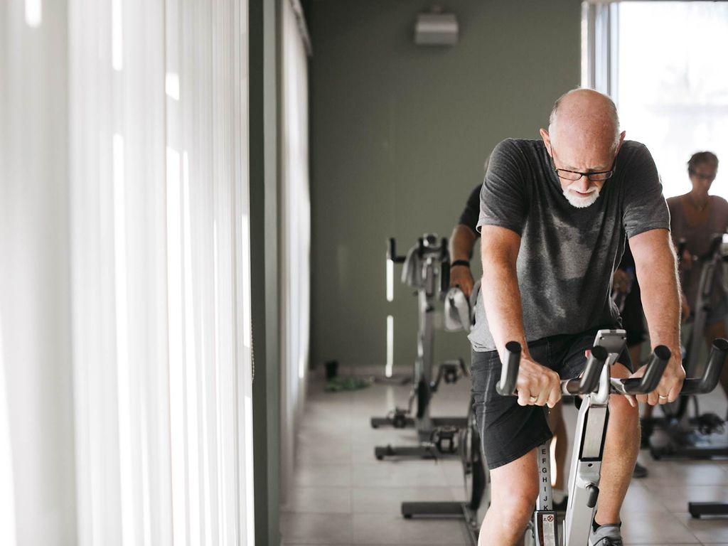 Schlaganfall: Älterer Mann auf Fahrradtrainer im Fitnessstudio.