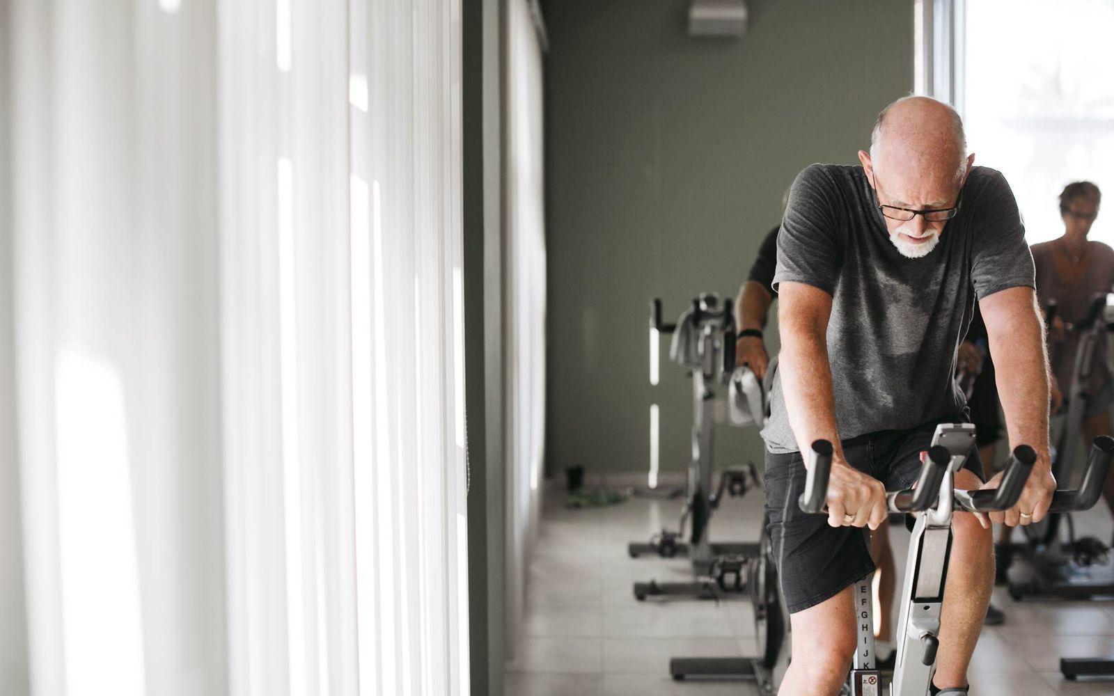 Schlaganfall: Älterer Mann auf Fahrradtrainer im Fitnessstudio.