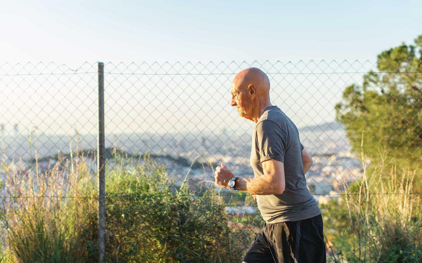 Koronare Herzkrankheit: Älterer Mann joggt, im Hintergrund ist ein Zaun und ein Stadtpanorama.