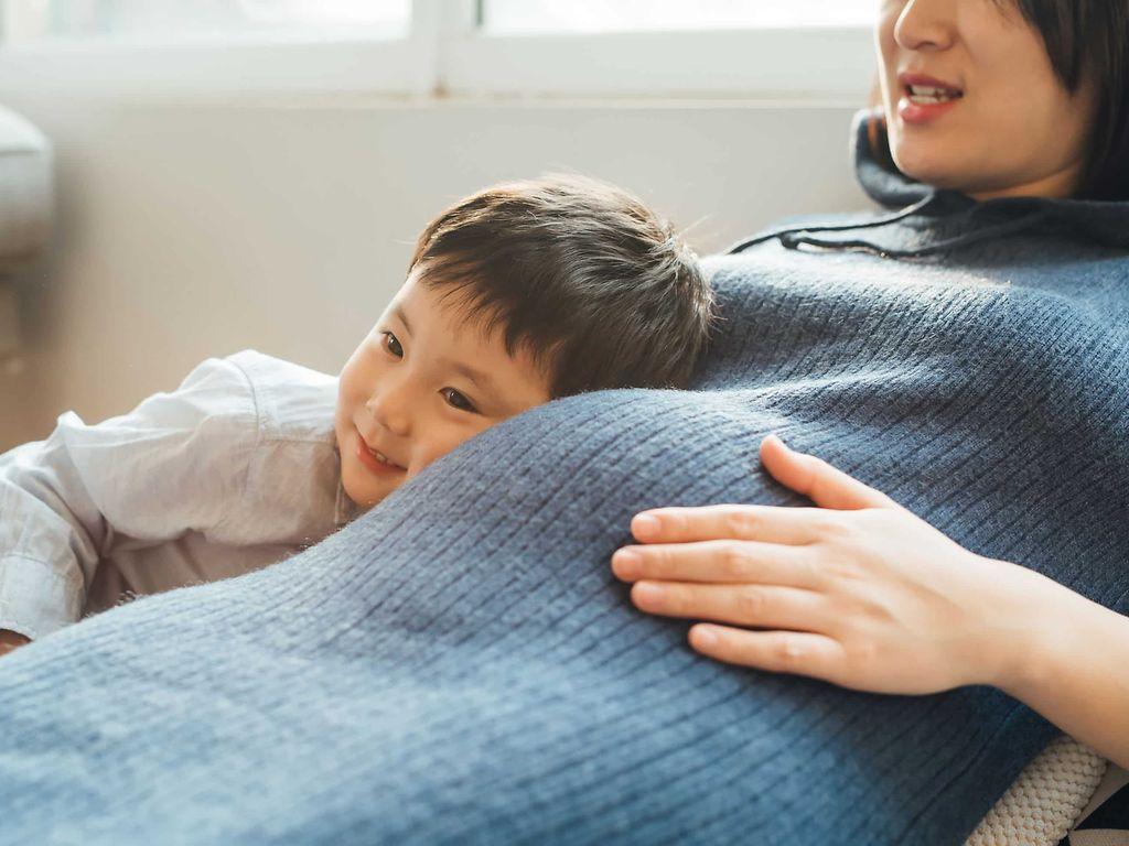 Ringelröteln Schwangerschaft: Kleiner Junge legt den Kopf an den Bauch einer Schwangeren.