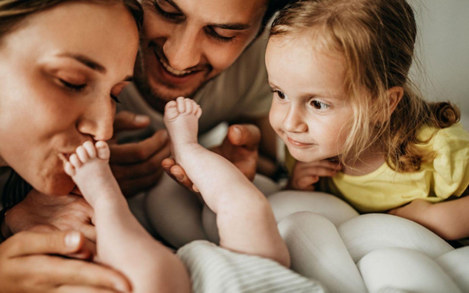 Symbolbild für Eifersucht unter Geschwistern: Eltern zeigen ihrem großen Kind das neue Baby