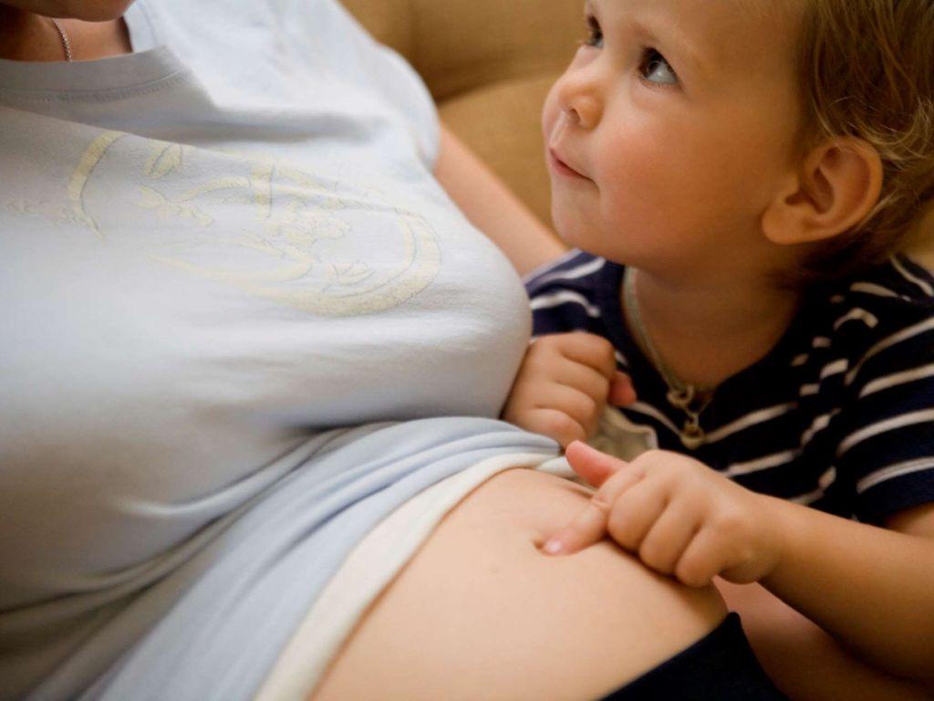 Meinen Bauch lieben: Ein Kind tippt mit seinem Finger auf den Bauch seiner Mutter.