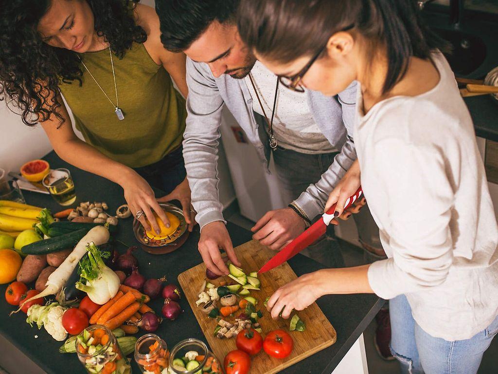 Sekundäre Pflanzenstoffe: Eine Gruppe von Freunden bereitet in der Küche vegetarisches Essen zu.